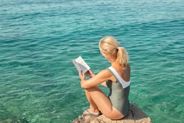 Kvinna sitter och läser en bok vid vattnet