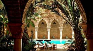 Innegården på La Sultana Marrakech, där två solstolar står under skuggande palmblad vid en liten pool.