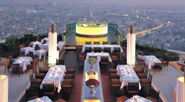 Dukade bord på takterrassen på Lebua at State Tower, med utsikt över Bangkok i skymningen.