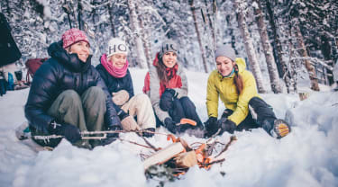 Fyra personer sitter i en snödriva framför en brasa