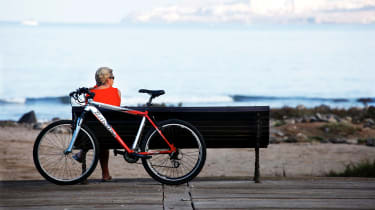 Cyklist som vilar på en bänk, med cykeln uppställd bakom sig