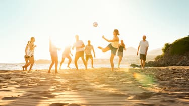 Familj spelar fotboll på stranden
