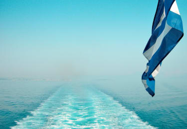 Grekisk flagga vajar i vinden efter en båt