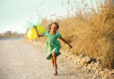 Barn springer på strand med ballonger