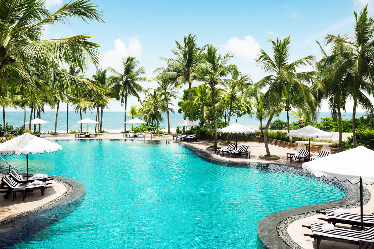 Vid hotellets mysiga poolområde skymtar havet mellan palmerna