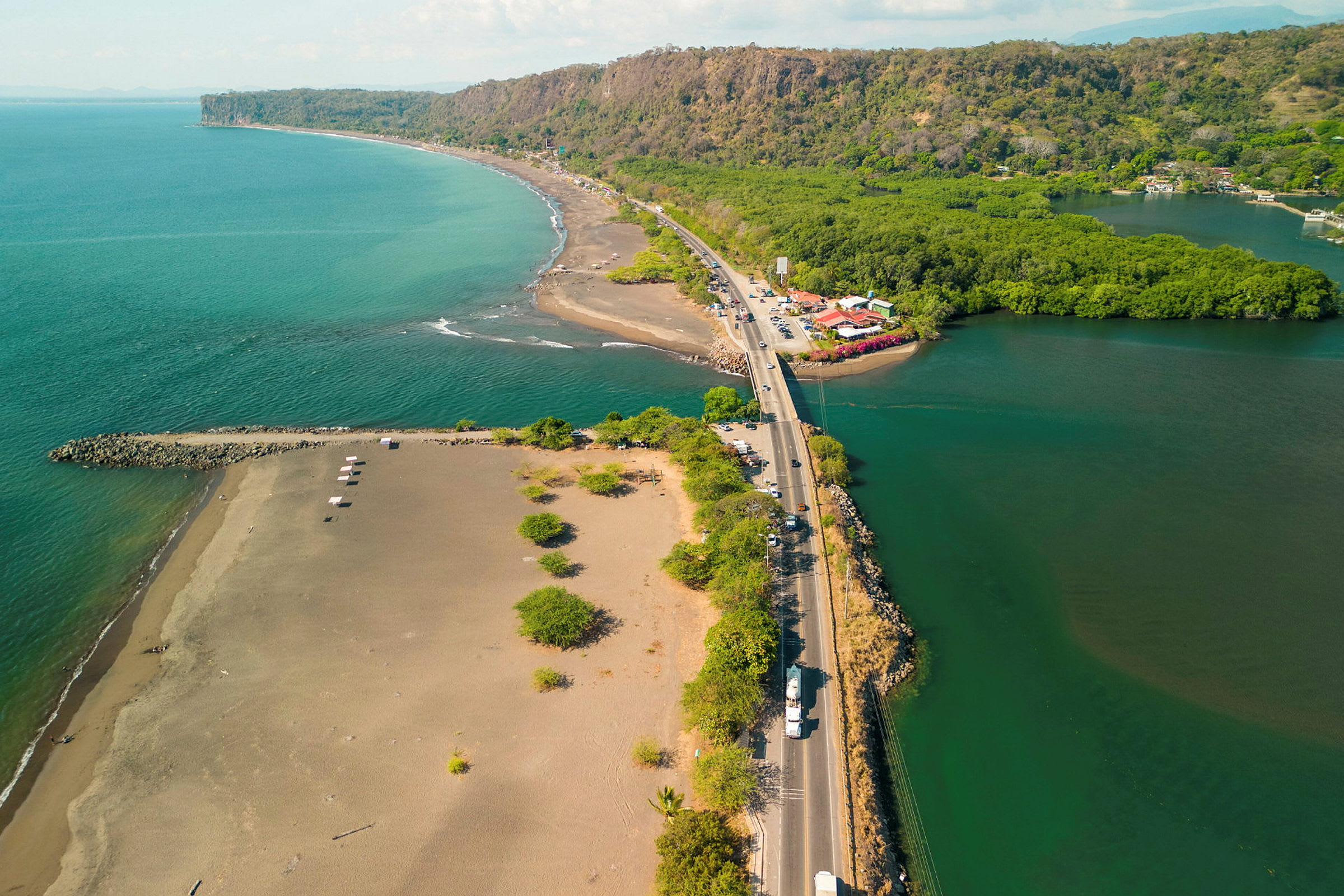 Luftbild av en sandstrand bredvid ett grönt kustlandskap med en väg som korsar området. (AI-genererad text)