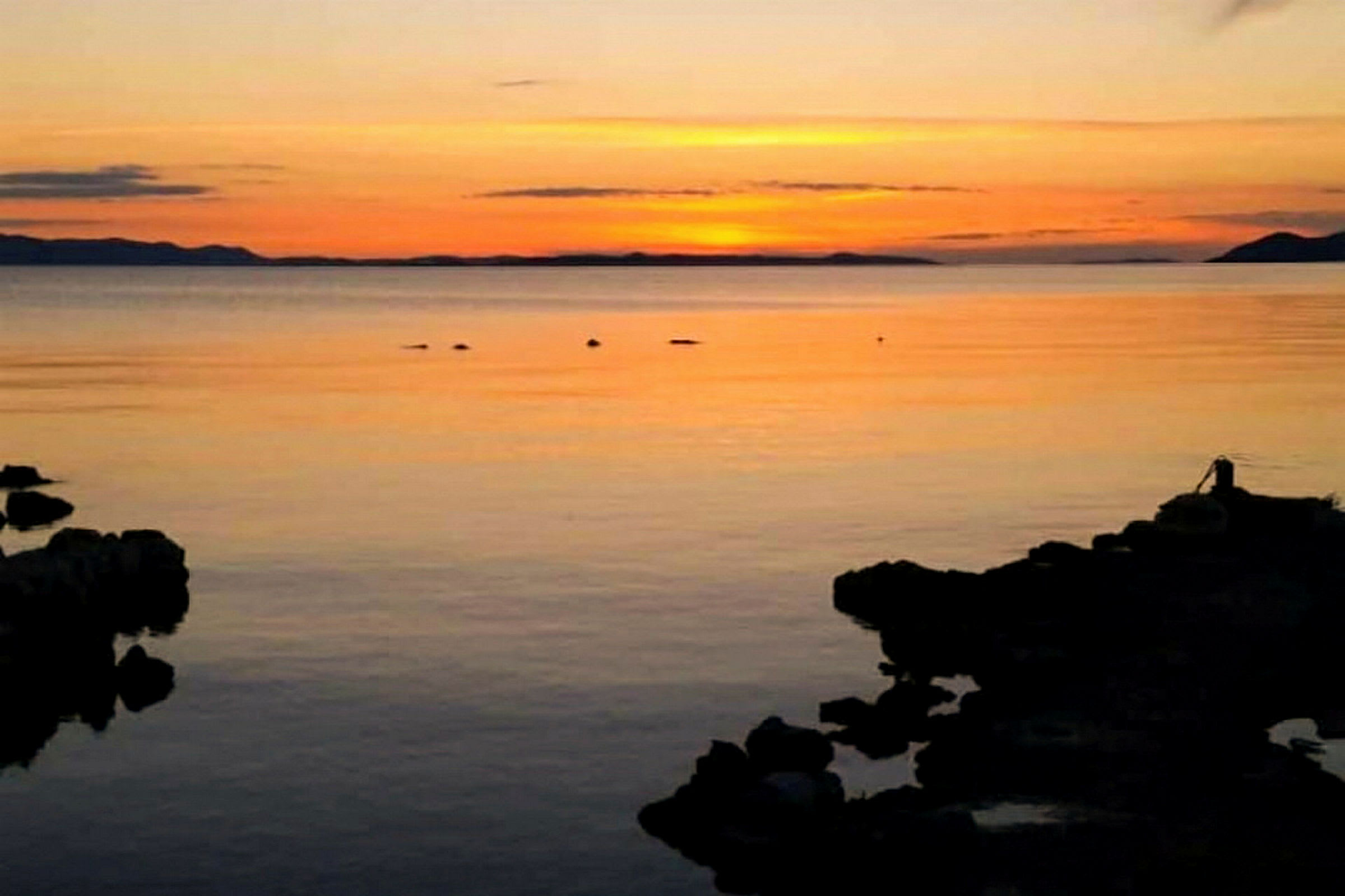 Solnedgång över ett stilla hav med silhuetter av klippor i förgrunden. (AI-genererad text)
