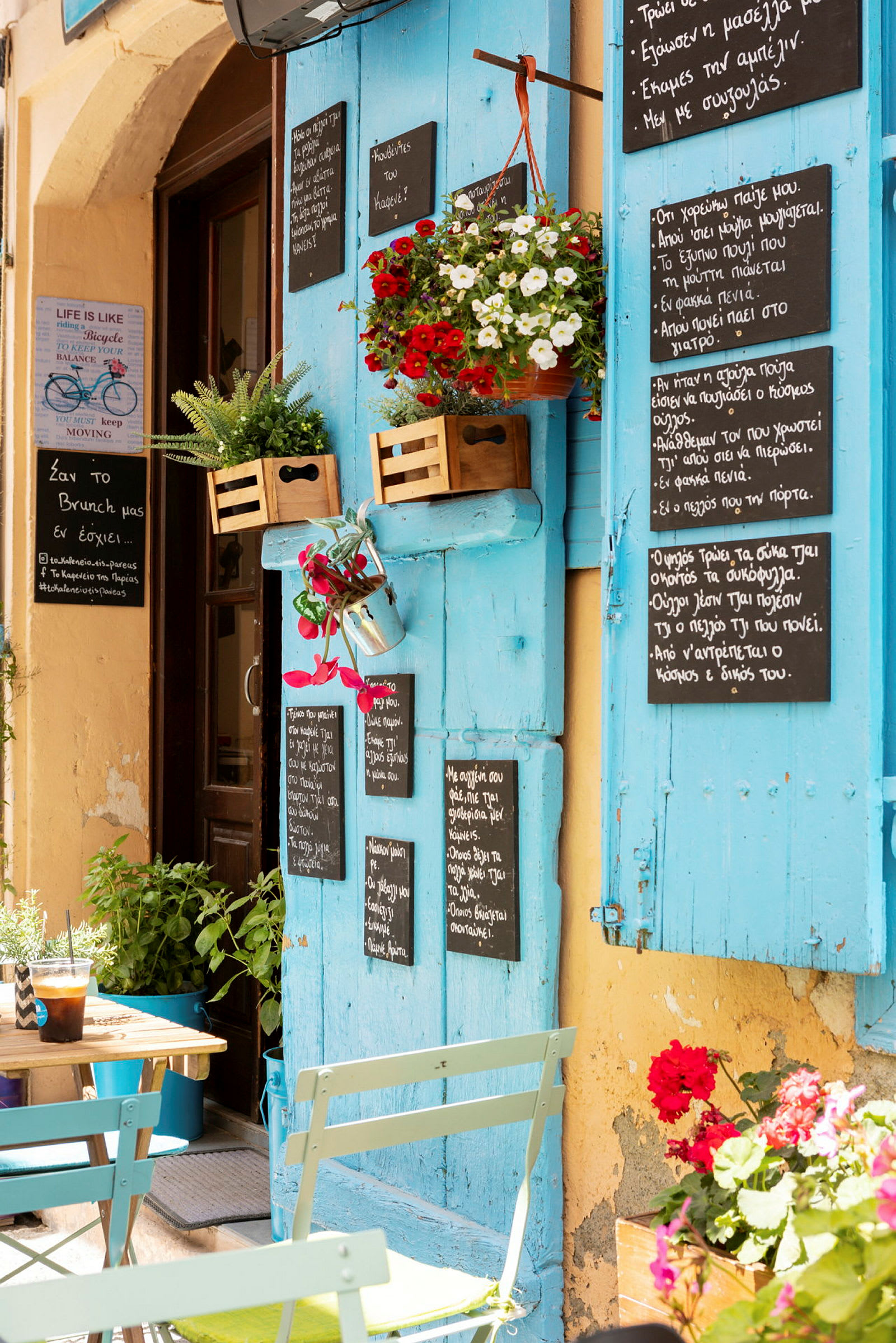 En färgglad cafémiljö med blå fönsterluckor, tavlor med text, och blommor. (AI-genererad text)