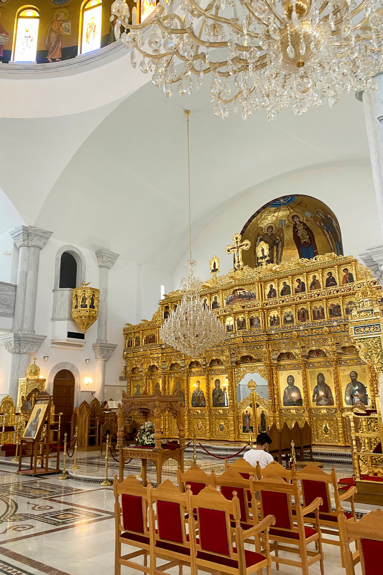 En interiörbild av en kyrka med en gyllene ikonostas, ikoner och en hängande kristallkrona. (AI-genererad text)