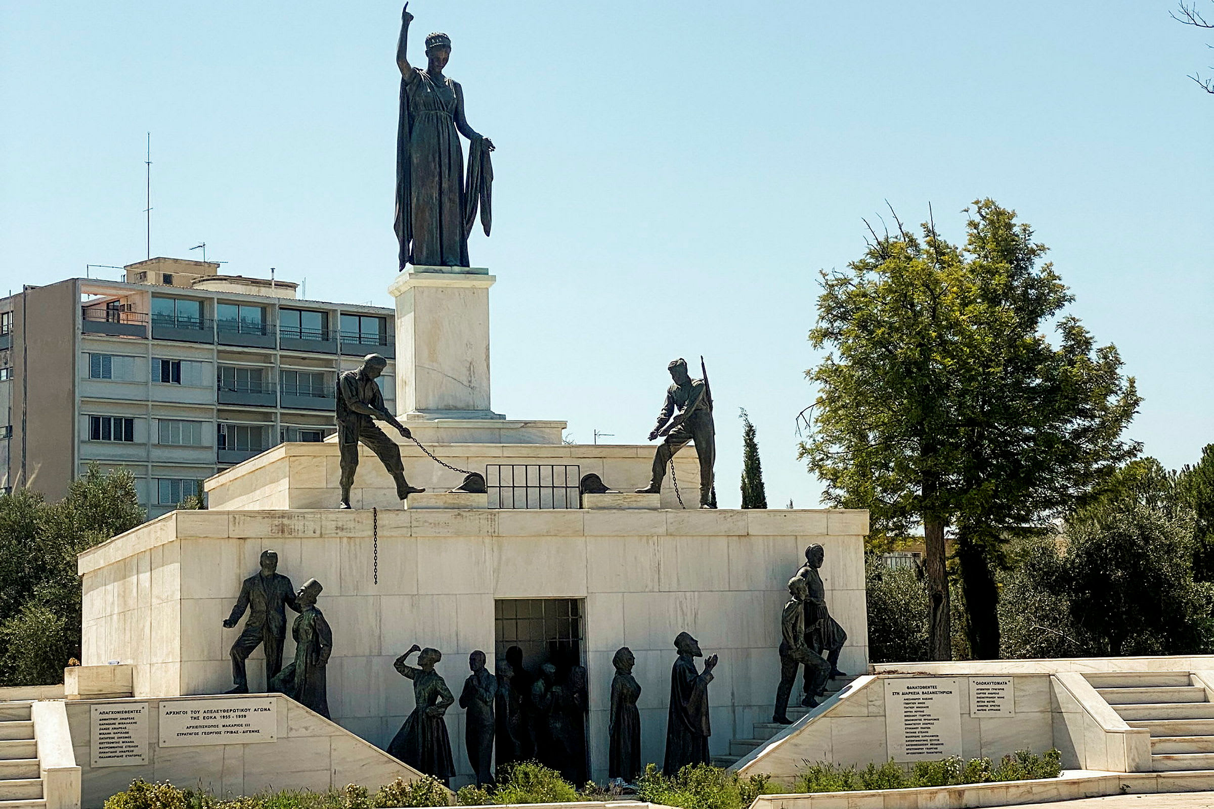 Ett monument i sten och brons med flera skulpturer som föreställer människor och en kvinna som håller en hand uppsträckt. (AI-genererad text)