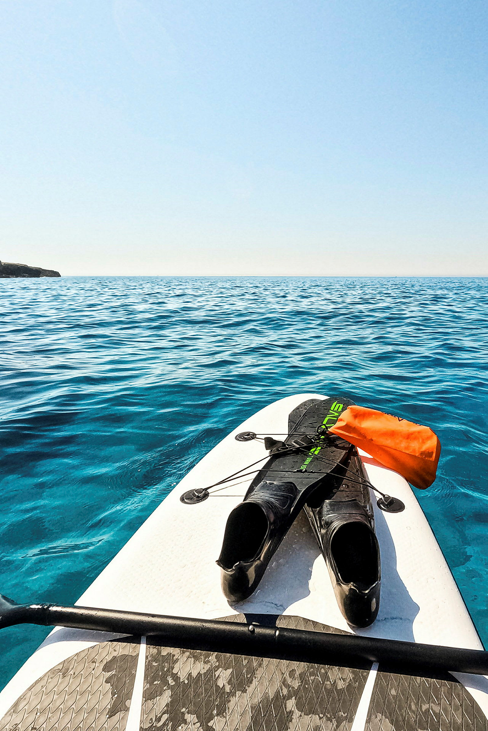 En paddleboard med simfenor och en orange vattentät påse fotograferad på ett lugnt hav. (AI-genererad text)