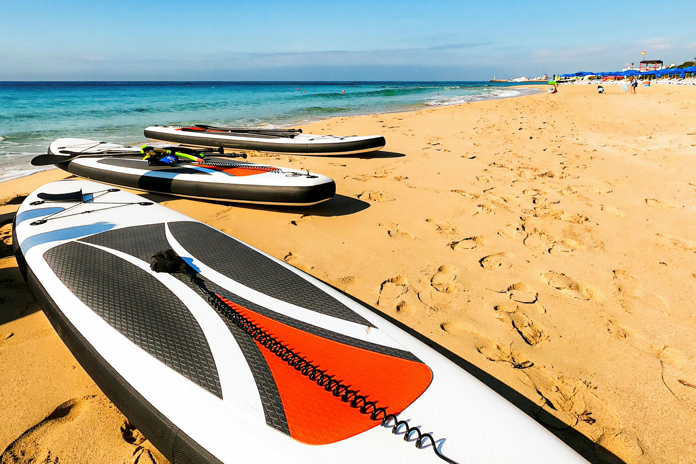 Bild av en sandstrand med flera stand up paddleboards placerade på sanden nära vattnet. (AI-genererad text)