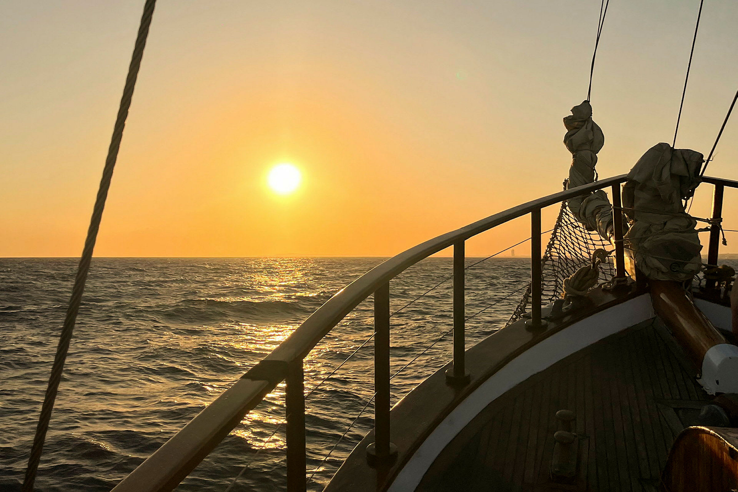 Solnedgång över havet med del av ett segelfartygs däck i förgrunden. (AI-genererad text)