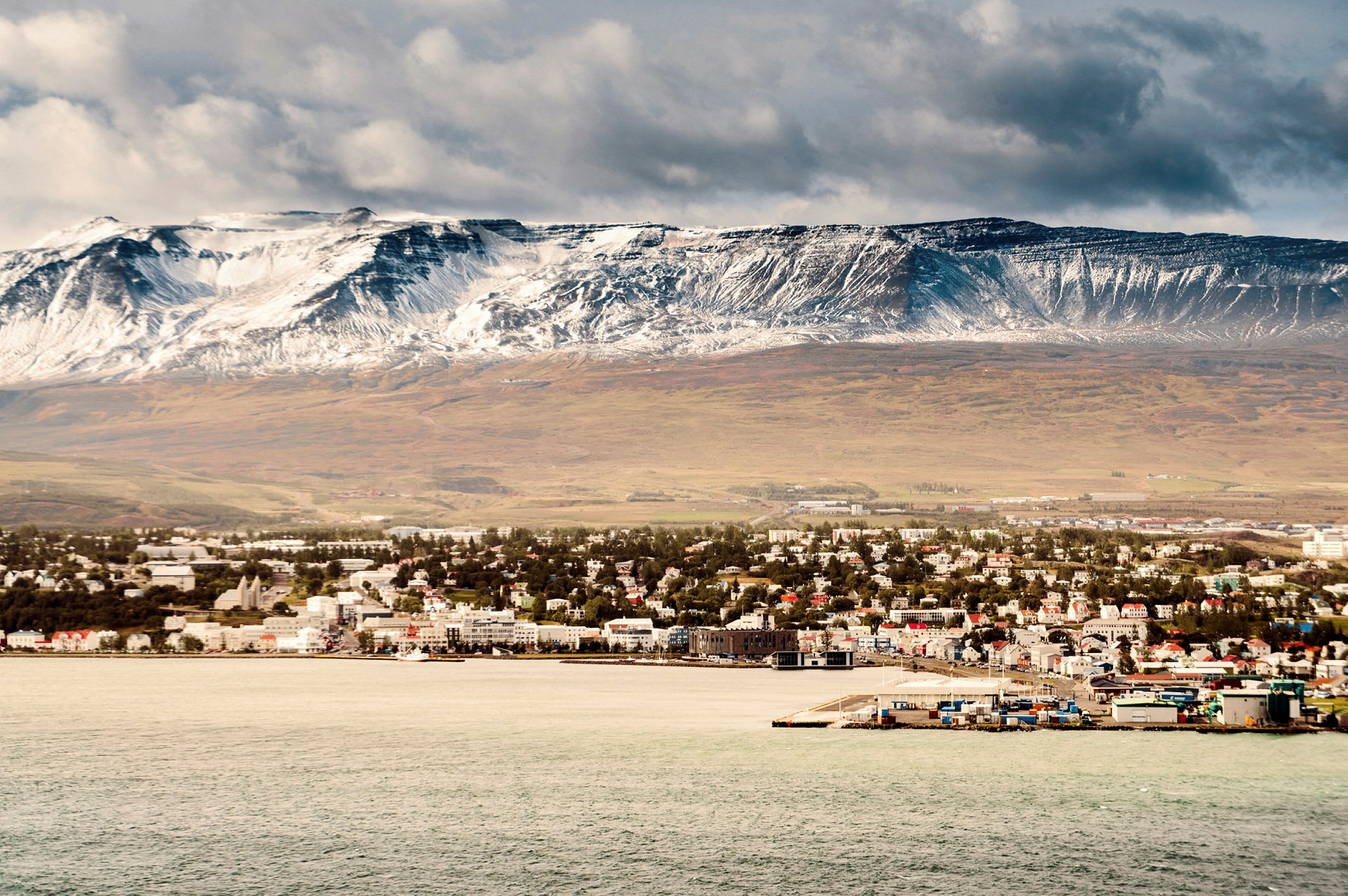 Vy över en kuststad med en snöklädd bergskedja i bakgrunden. (AI-genererad text)