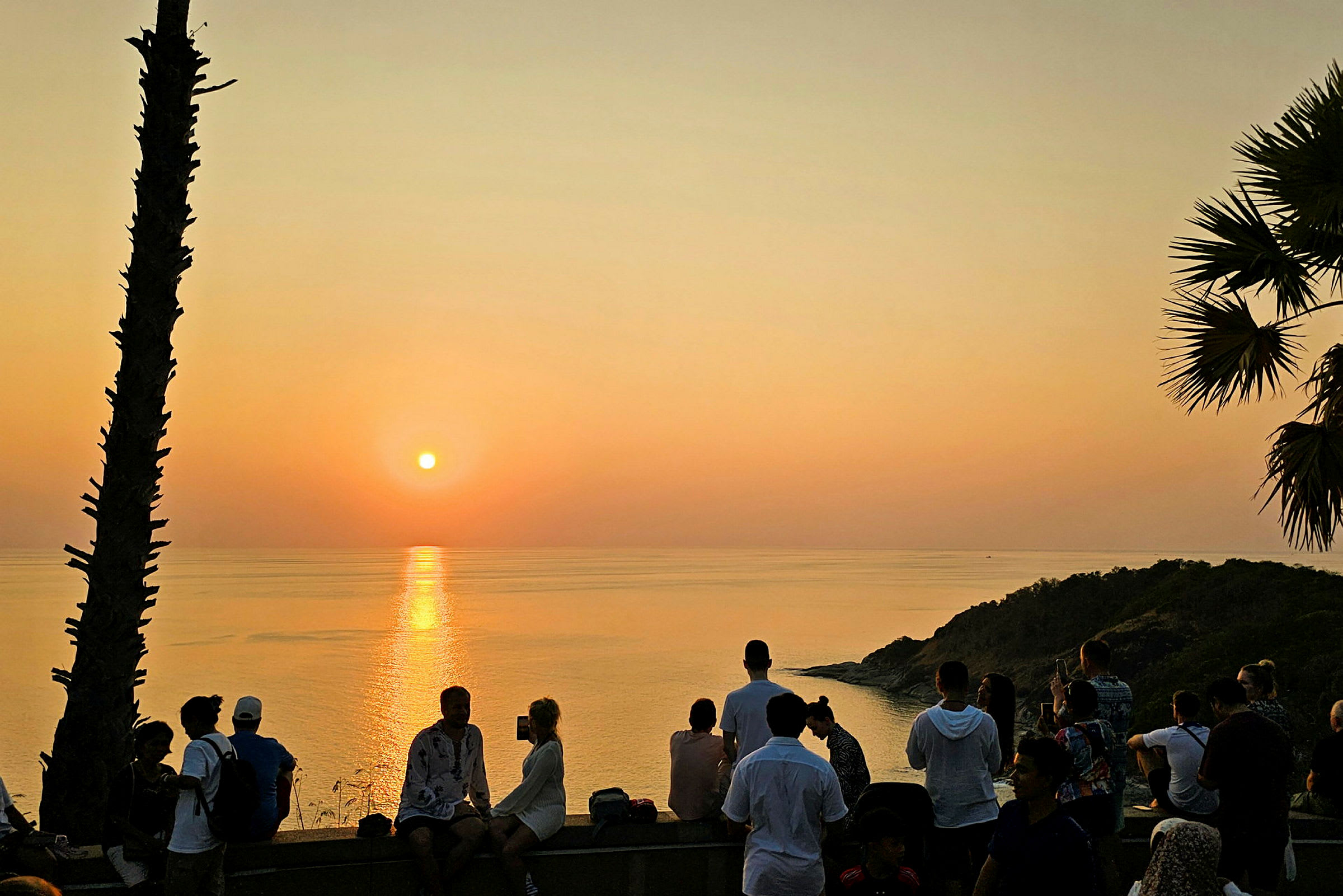 Solnedgång över havet med människor som samlats på en utsiktsplats. (AI-genererad text)