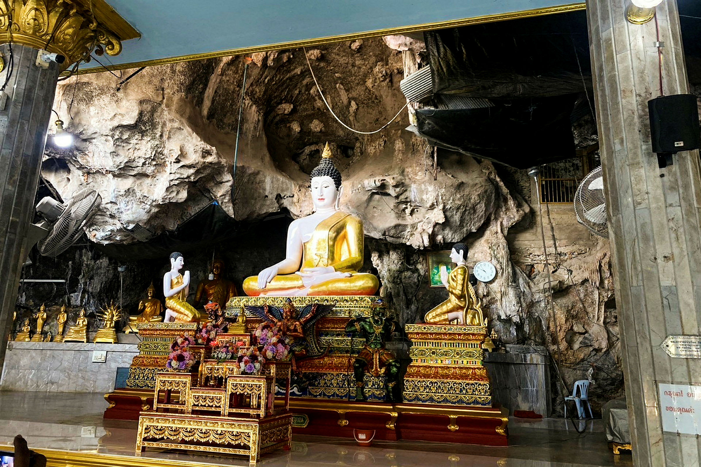 Bilden visar en buddhastaty i en dekorerad miljö med klippväggar. (AI-genererad text)