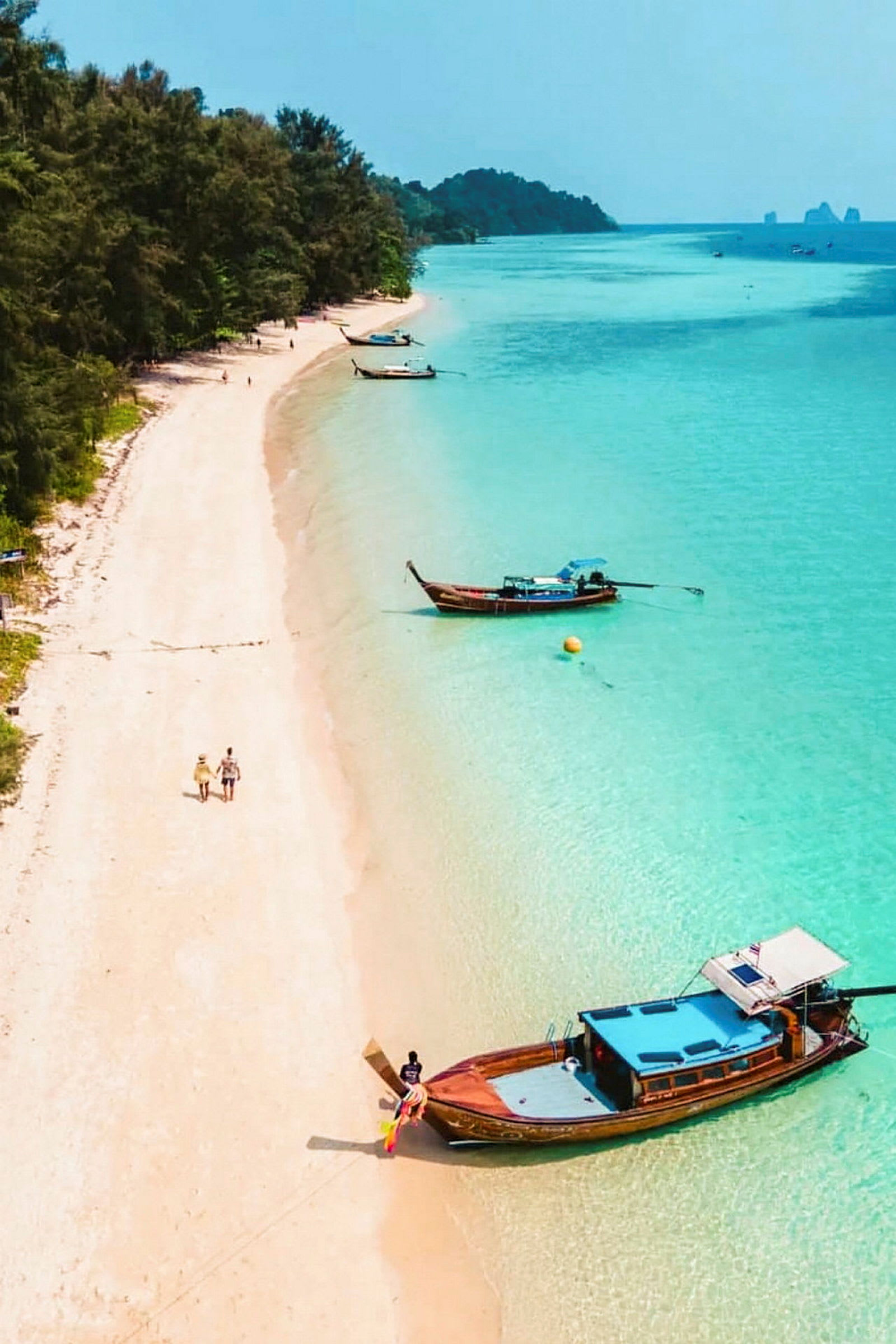 Bilden visar en gyllene strand med klara turkosa vatten och träbåtar nära stranden. (AI-genererad text)
