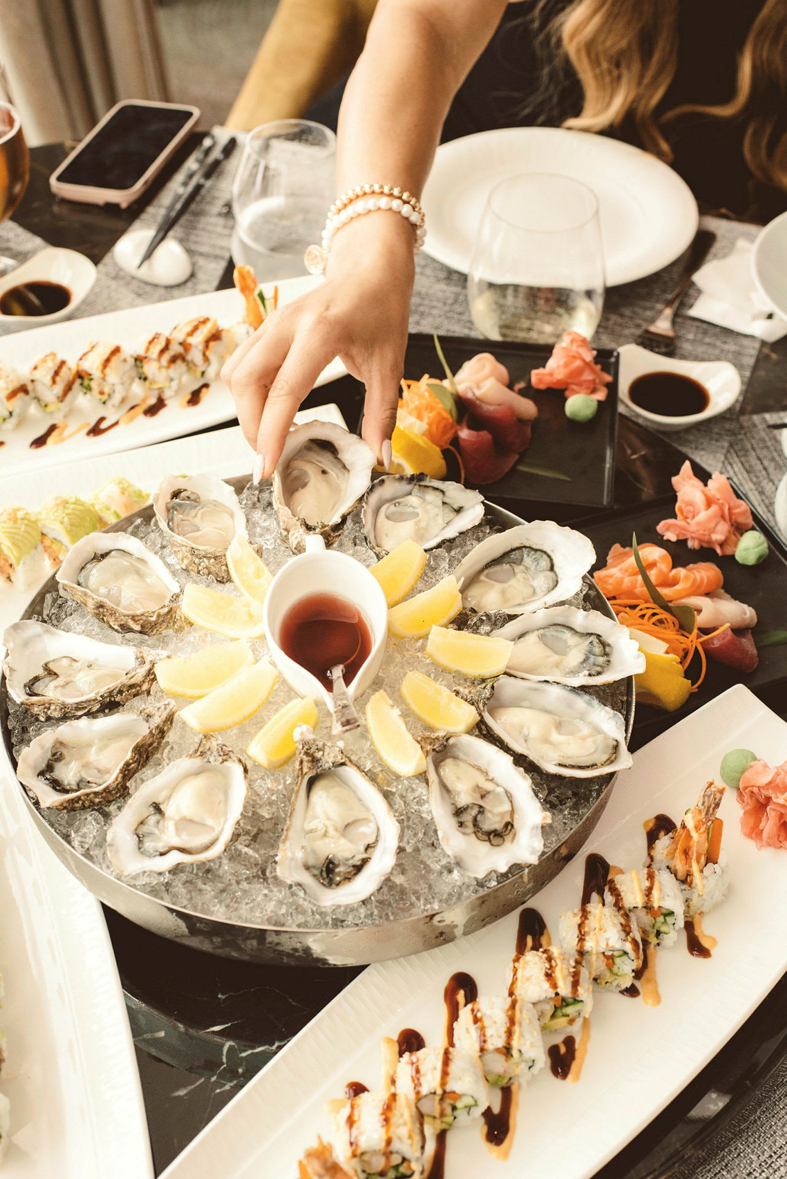 En tallrik med ostron serverade på is med citronklyftor i mitten, tillsammans med sushi och sashimi på andra tallrikar. (AI-genererad text)