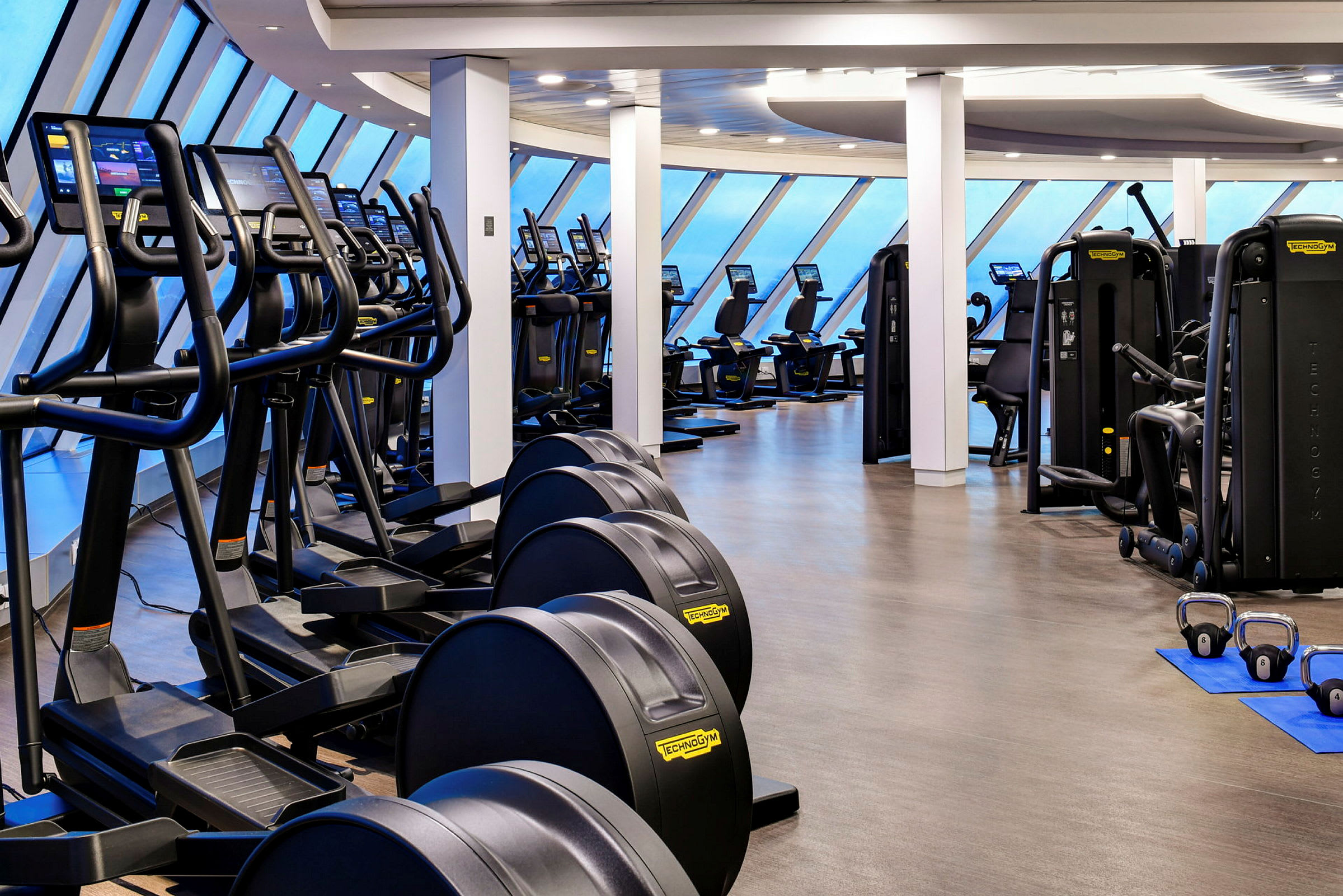 Bild av ett gym utrustat med olika träningsmaskiner och fönster mot en blå himmel. (AI-genererad text)