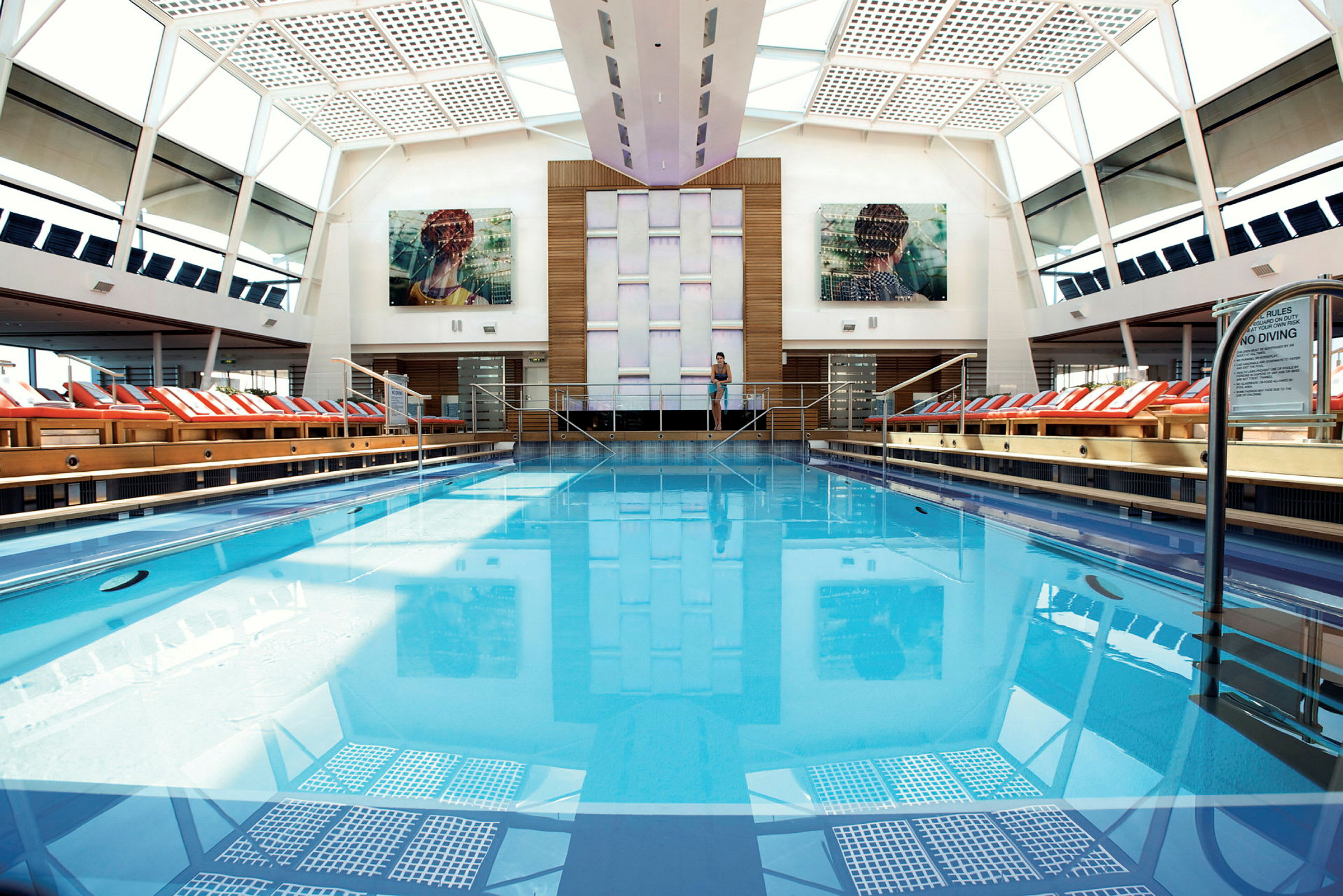 Inomhuspool med klarblått vatten omgiven av solstolar, under ett glastak. (AI-genererad text)