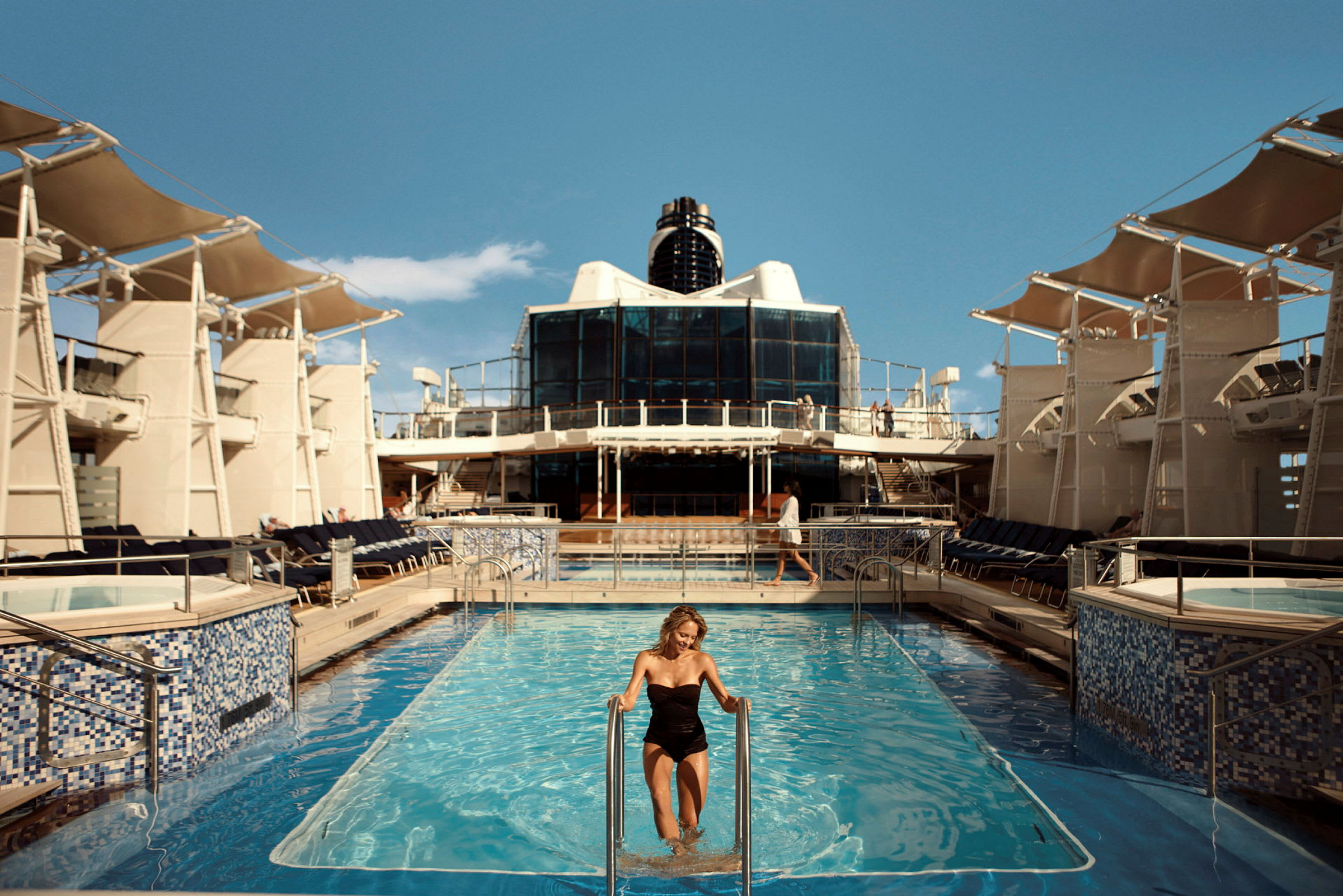 En person går upp ur en pool på ett fartyg, med solstolar och tak över sidorna. (AI-genererad text)