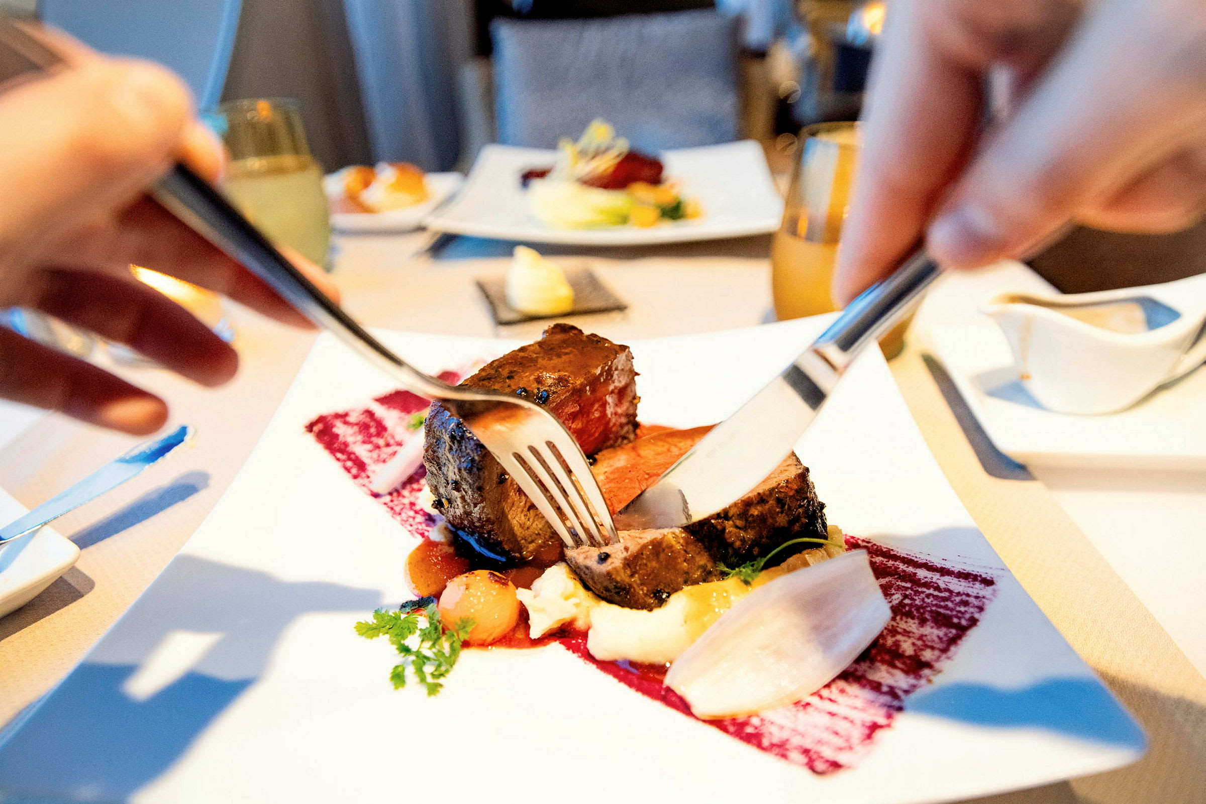 En tallrik med mat där någon skär kött med kniv och gaffel. (AI-genererad text)
