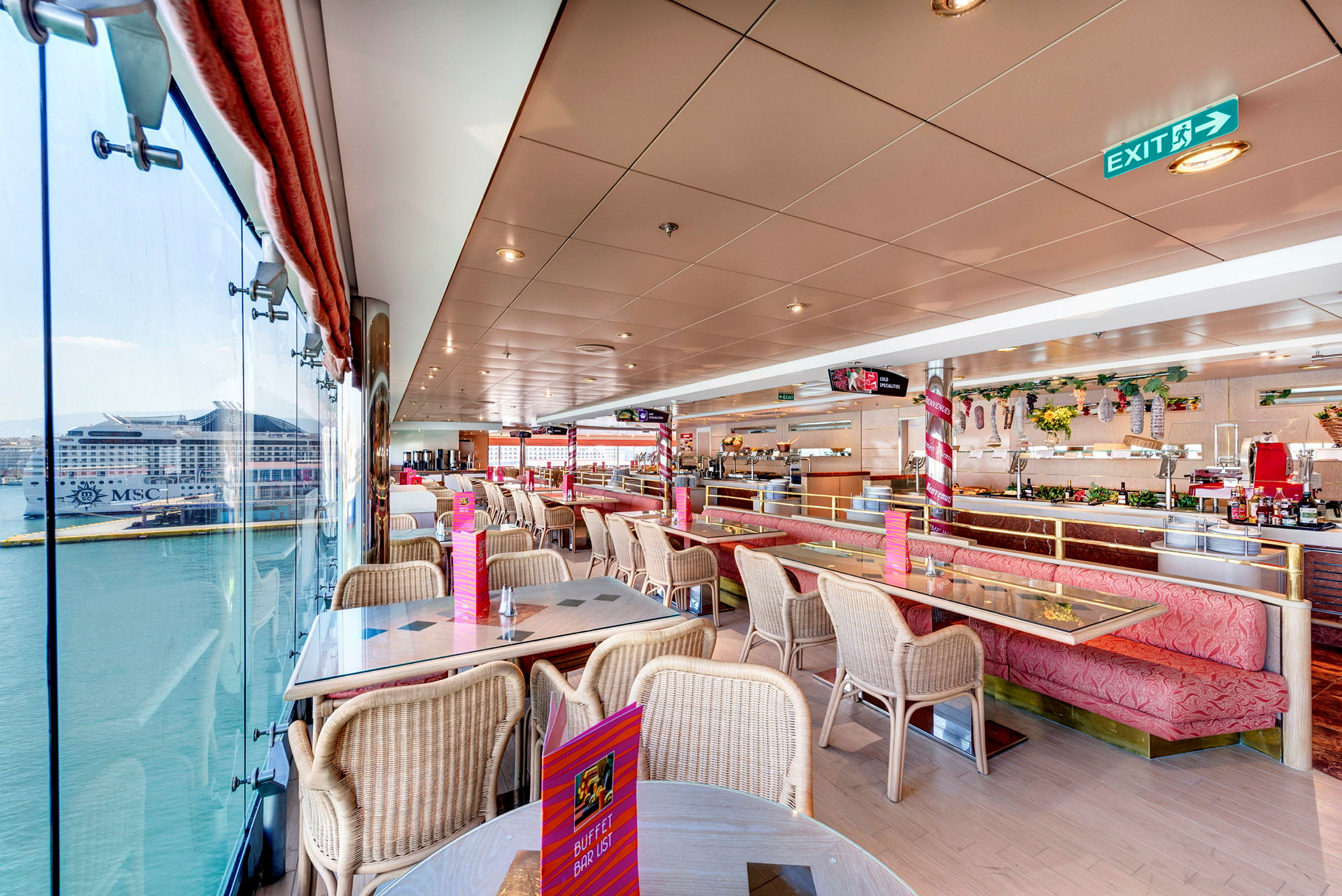 Inomhusbild av en ljus restaurang med sittplatser och stora fönster med utsikt mot ett fartyg i en hamn. (AI-genererad text)