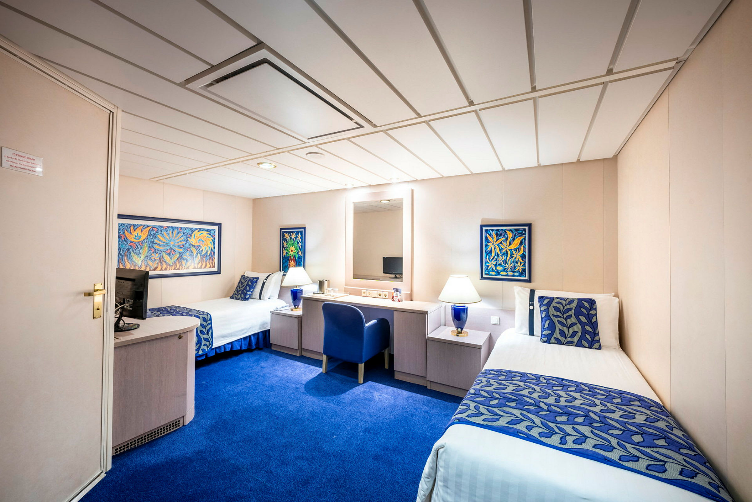 Hotellrum med två enkelsängar, blå inredning och bord mellan sängarna. Väggdekoration i färg finns. (AI-genererad text)