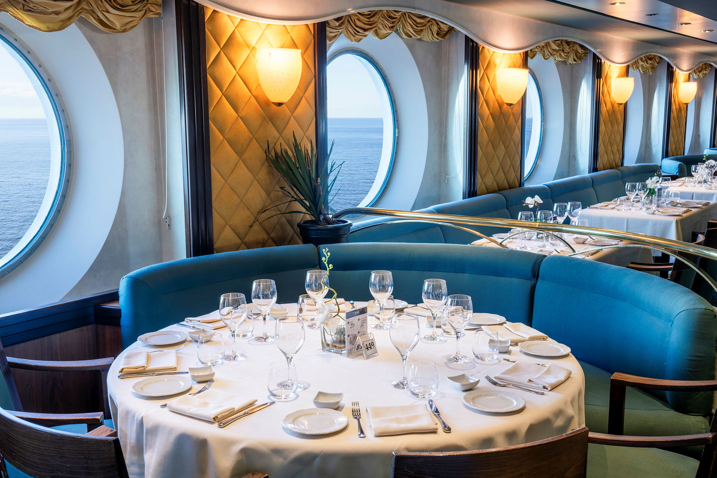 En restaurang med dukade bord, blå soffor och stora runda fönster som visar havsutsikten. (AI-genererad text)