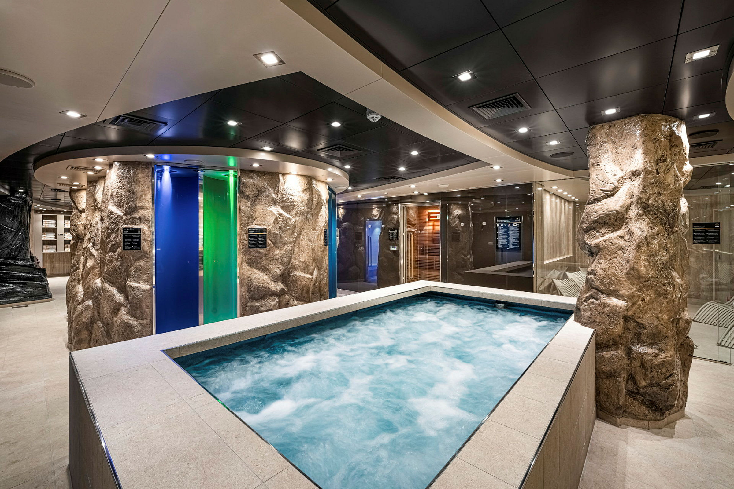 Ett spaområde med en jacuzzi omgiven av stenliknande pelare och färgade glasdörrar. (AI-genererad text)