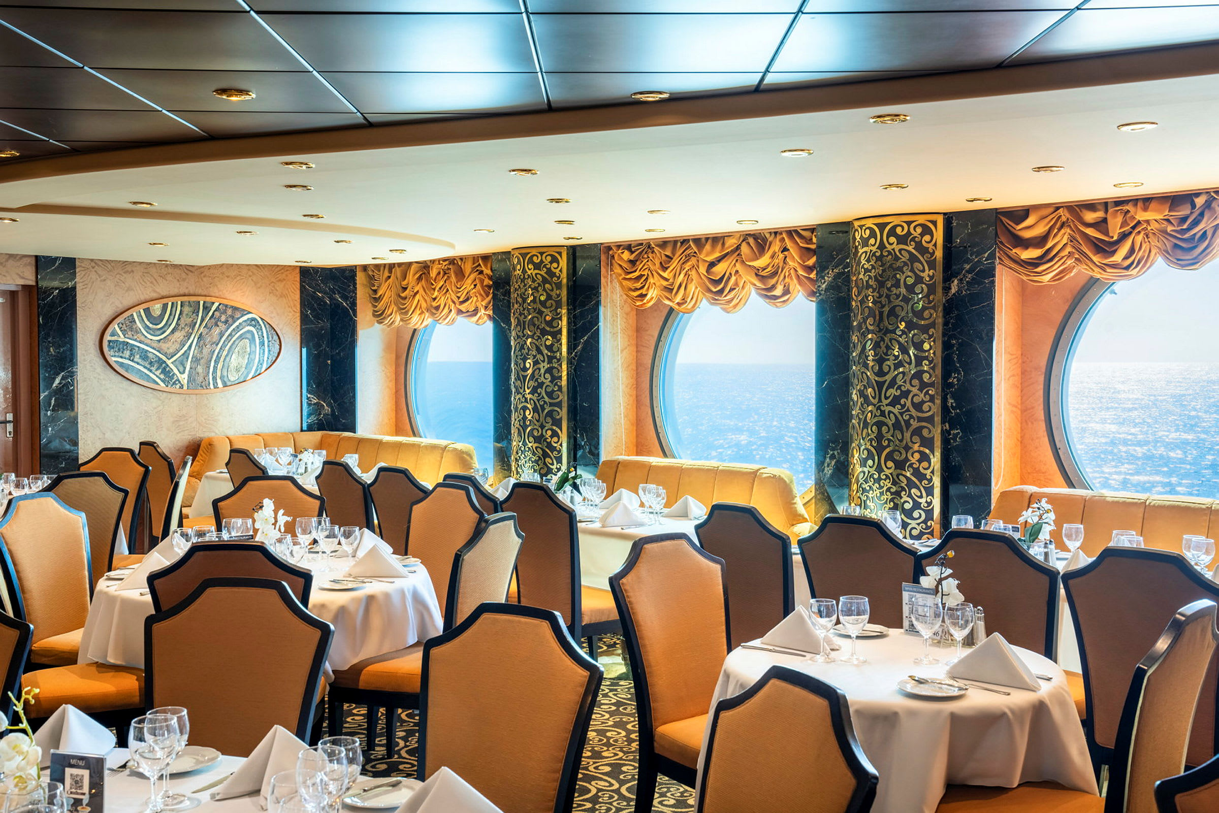 En elegant restaurang med dukade bord, beige stolar och stora fönster med havsutsikt. (AI-genererad text)