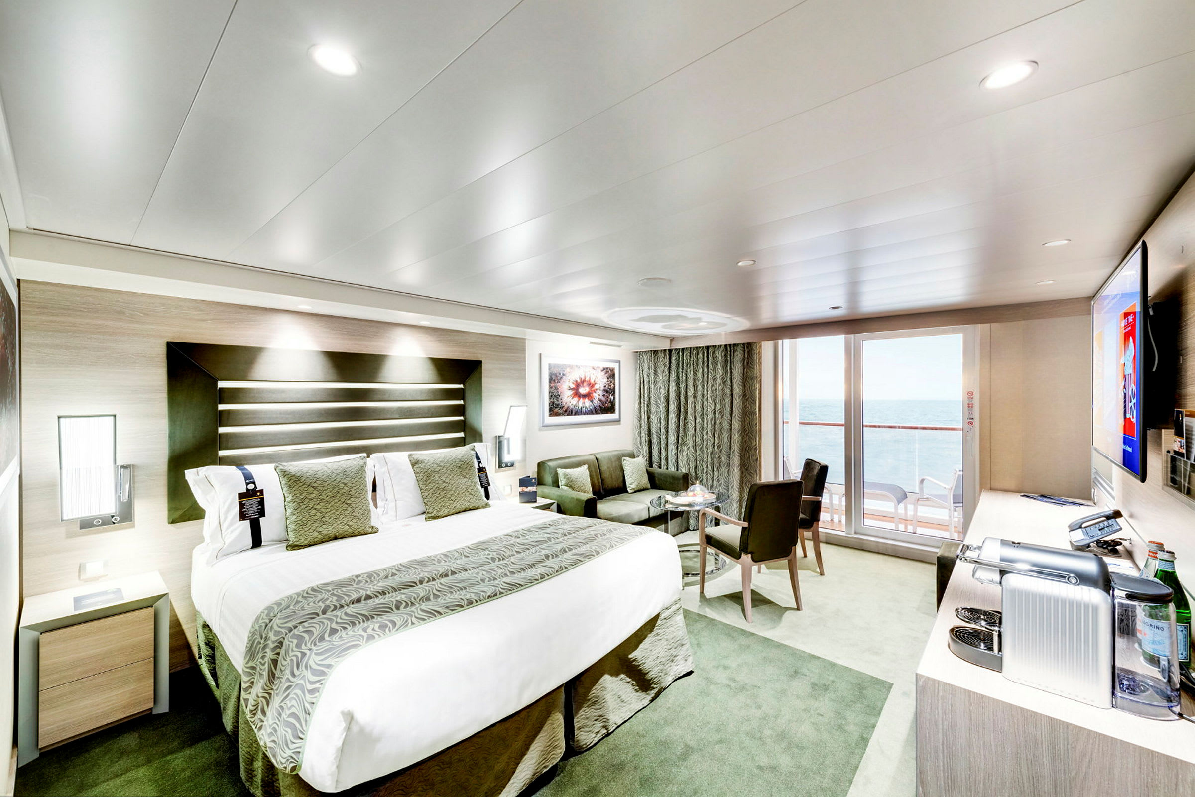 Modern hotellrum med stor säng, sittgrupp, och balkong med havsutsikt. (AI-genererad text)