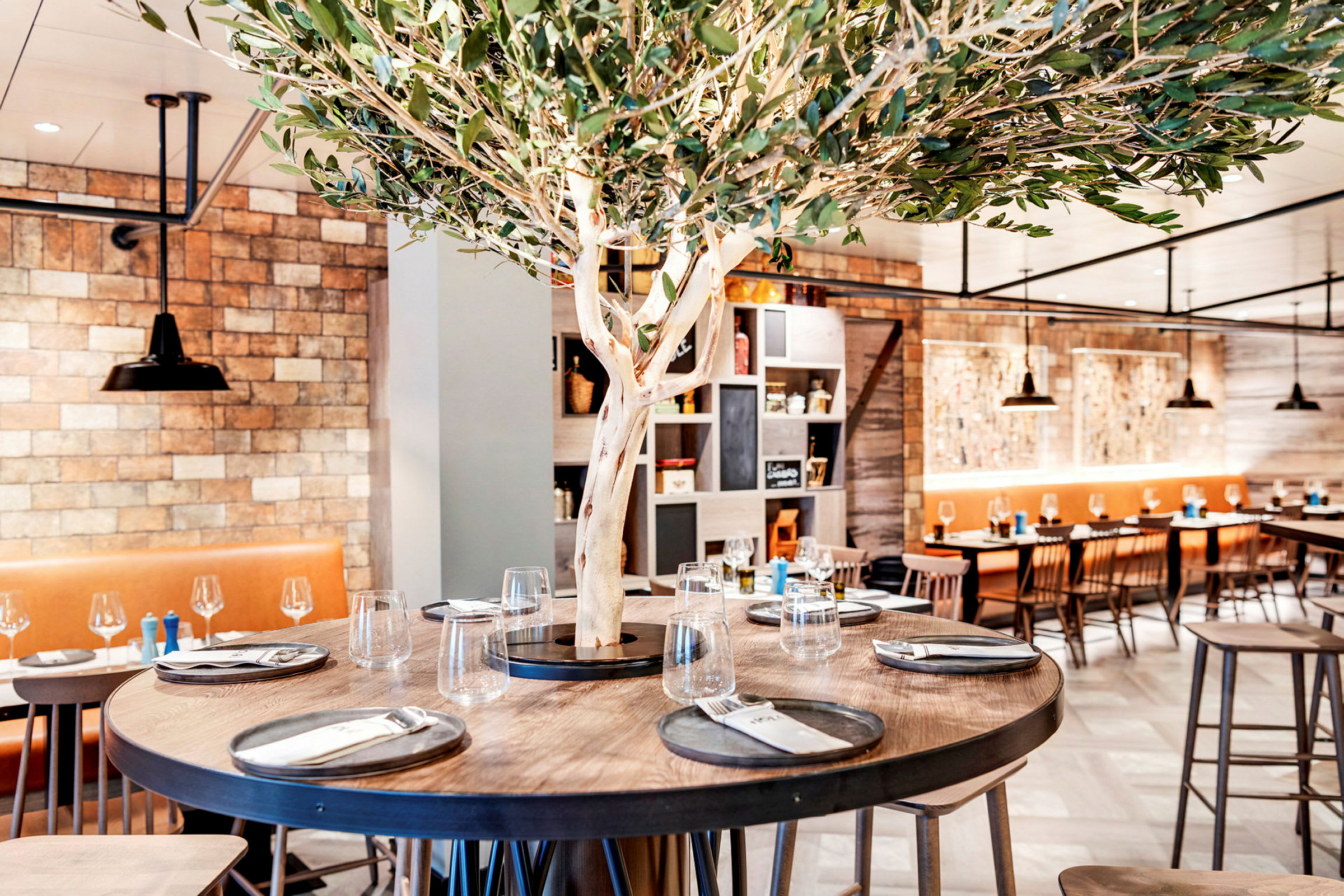 Ett modern restaurangområde med ett runt bord dekorerat med en trädstam och dukade tallrikar. (AI-genererad text)