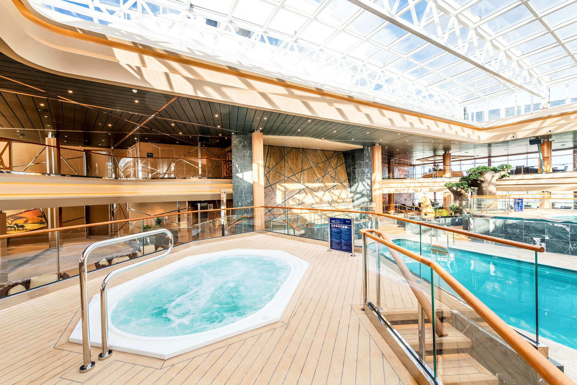 Interiörbild av ett ljust utrymme med en jacuzzi och en pool, omgiven av glasräcken. (AI-genererad text)