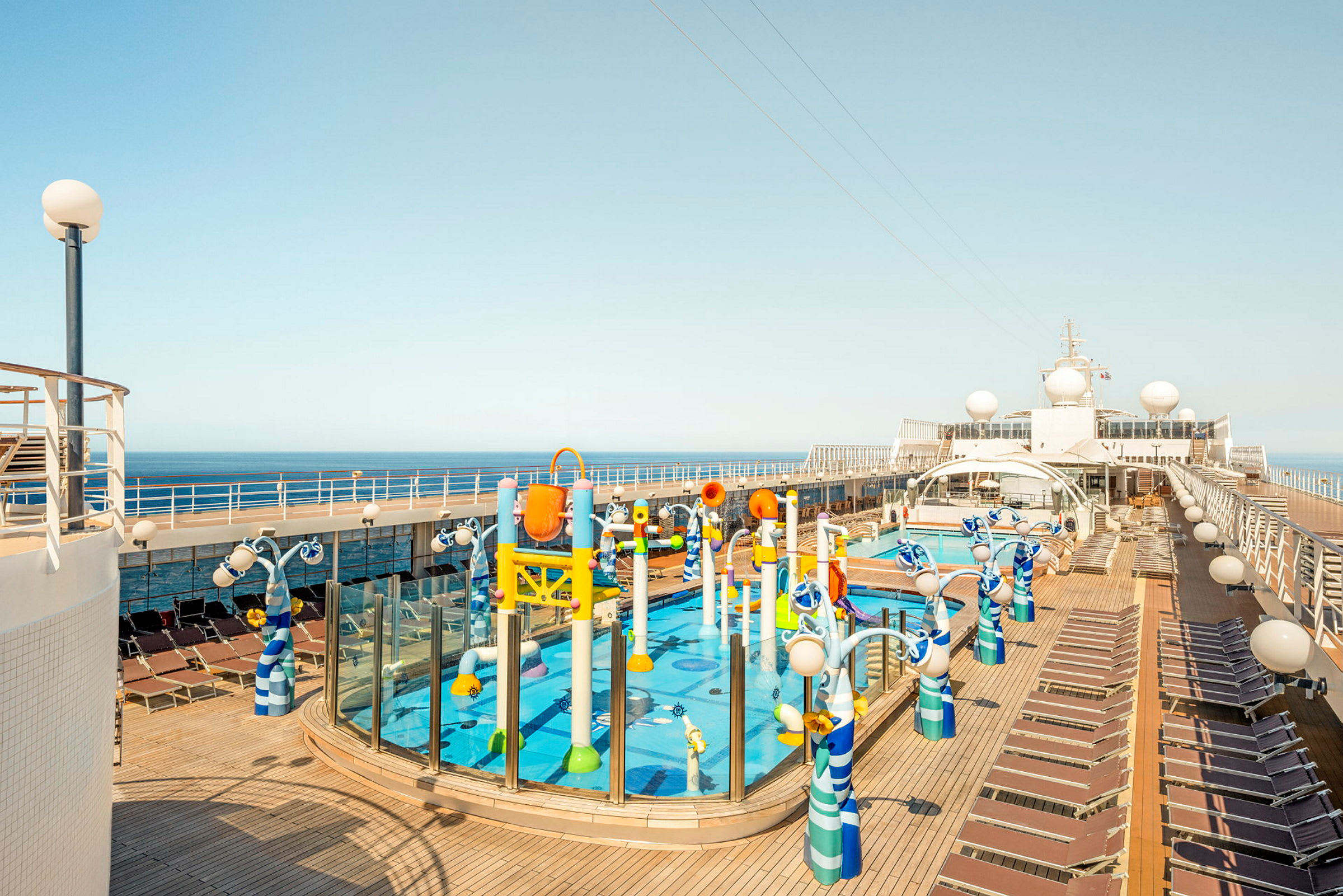 En bild på ett kryssningsfartygs utomhusdäck med pool, vattenlek och solstolar. (AI-genererad text)