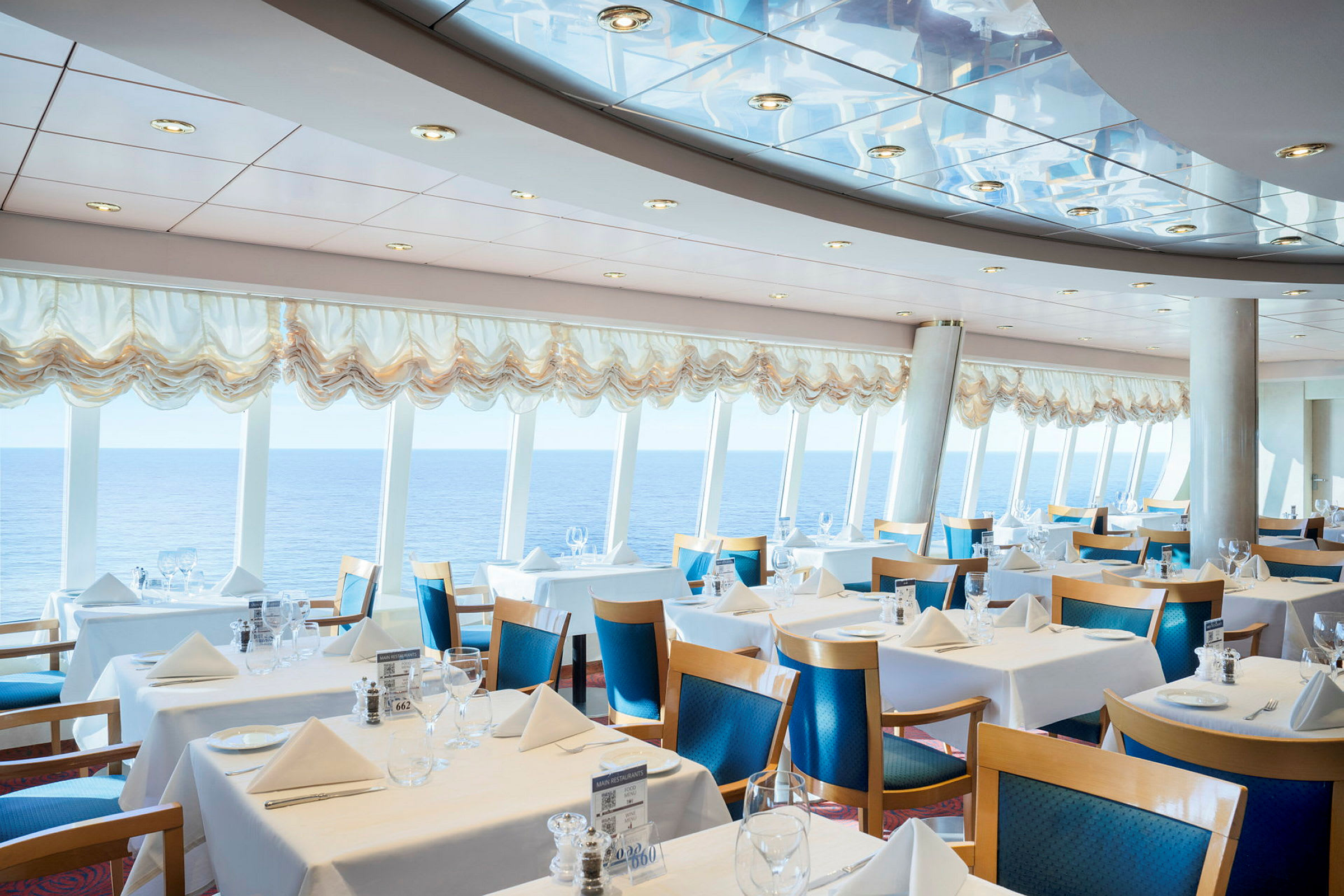 Restaurang med dukade bord, havsutsikt och stora fönster. (AI-genererad text)