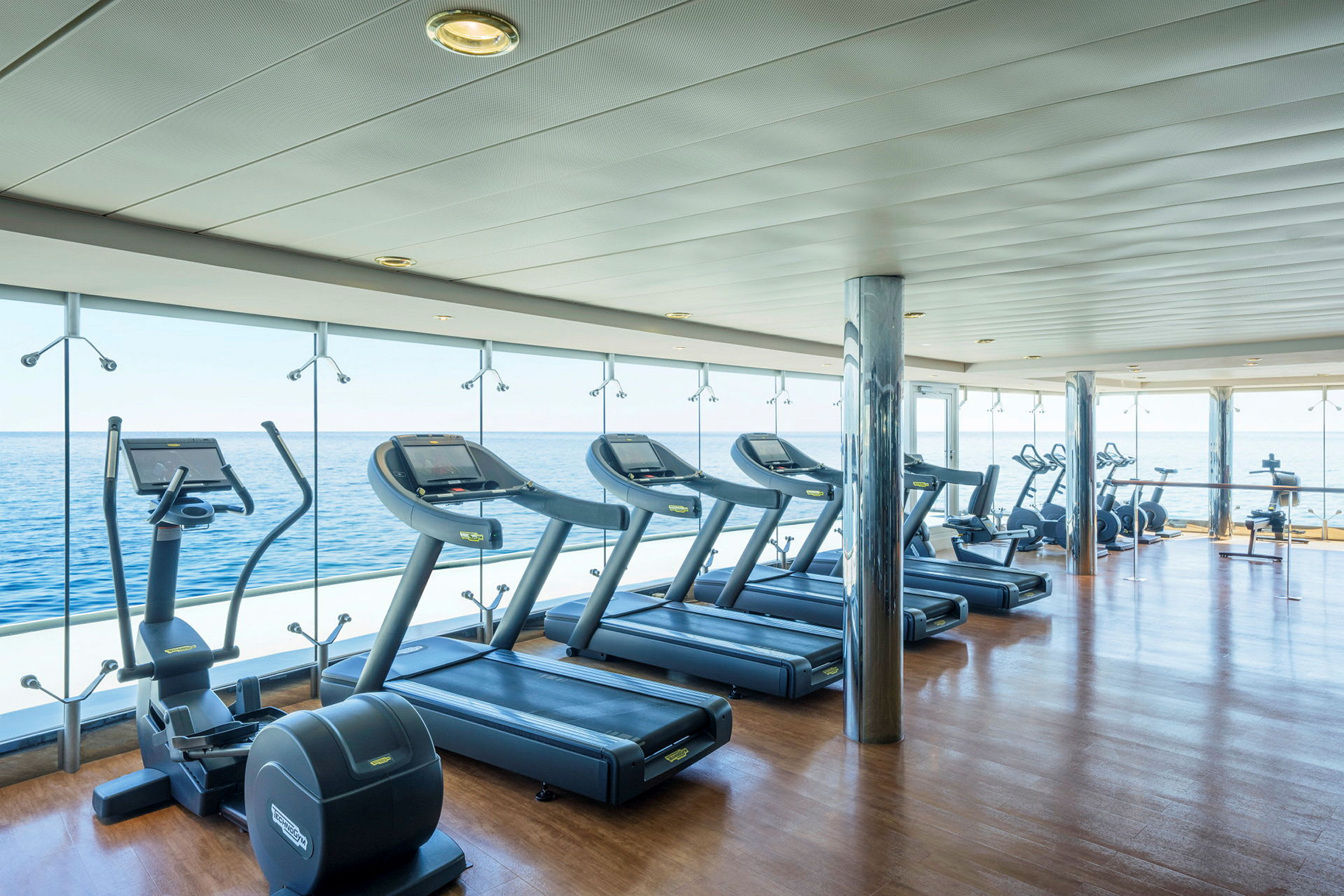 Bild av ett gym med träningsmaskiner vid stora fönster som ger en utsikt över havet. (AI-genererad text)