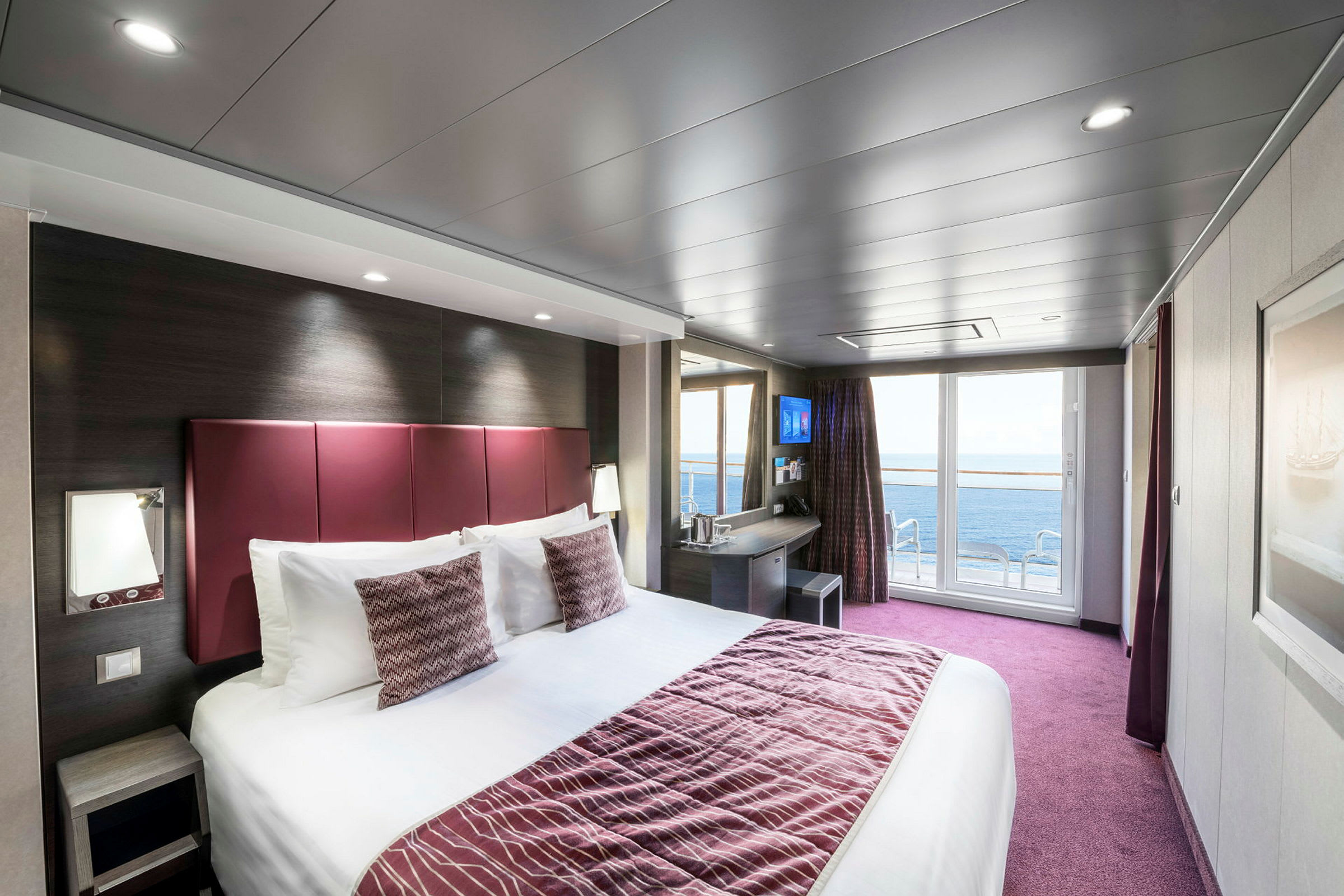 Interiör av ett hotellrum med en stor säng, arbetsyta och balkong med havsutsikt. (AI-genererad text)