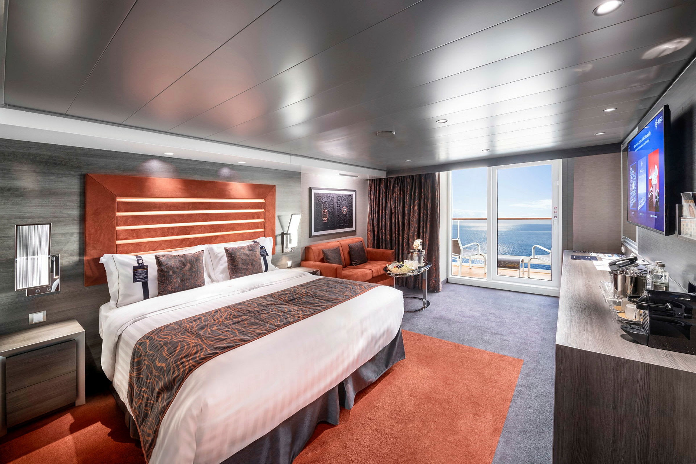 Ett hotellrum med en stor säng, en sittgrupp och utsikt mot havet från en balkong. (AI-genererad text)