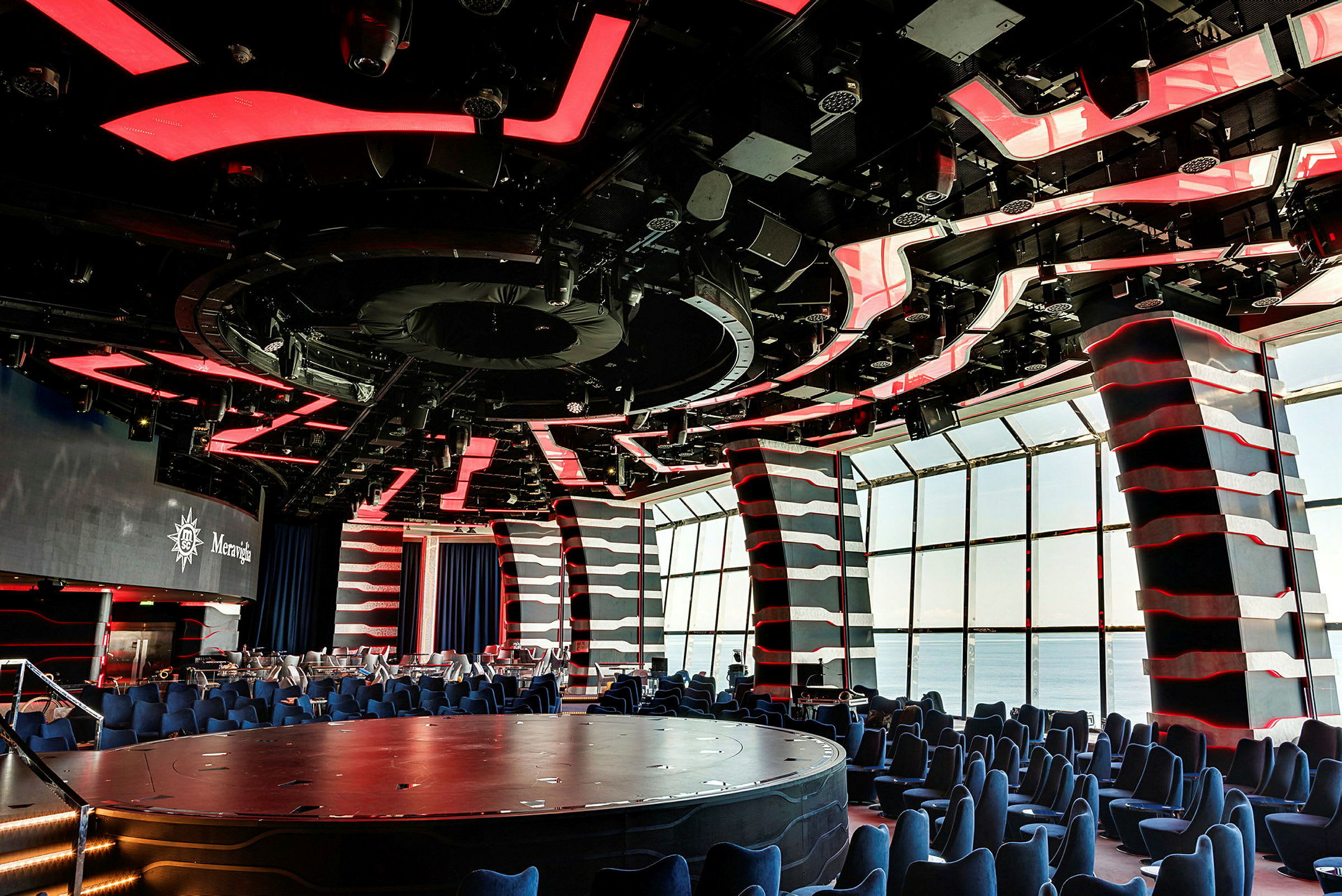Ett modernt auditorium med rött och svart tak, sittplatser och stora fönster. (AI-genererad text)