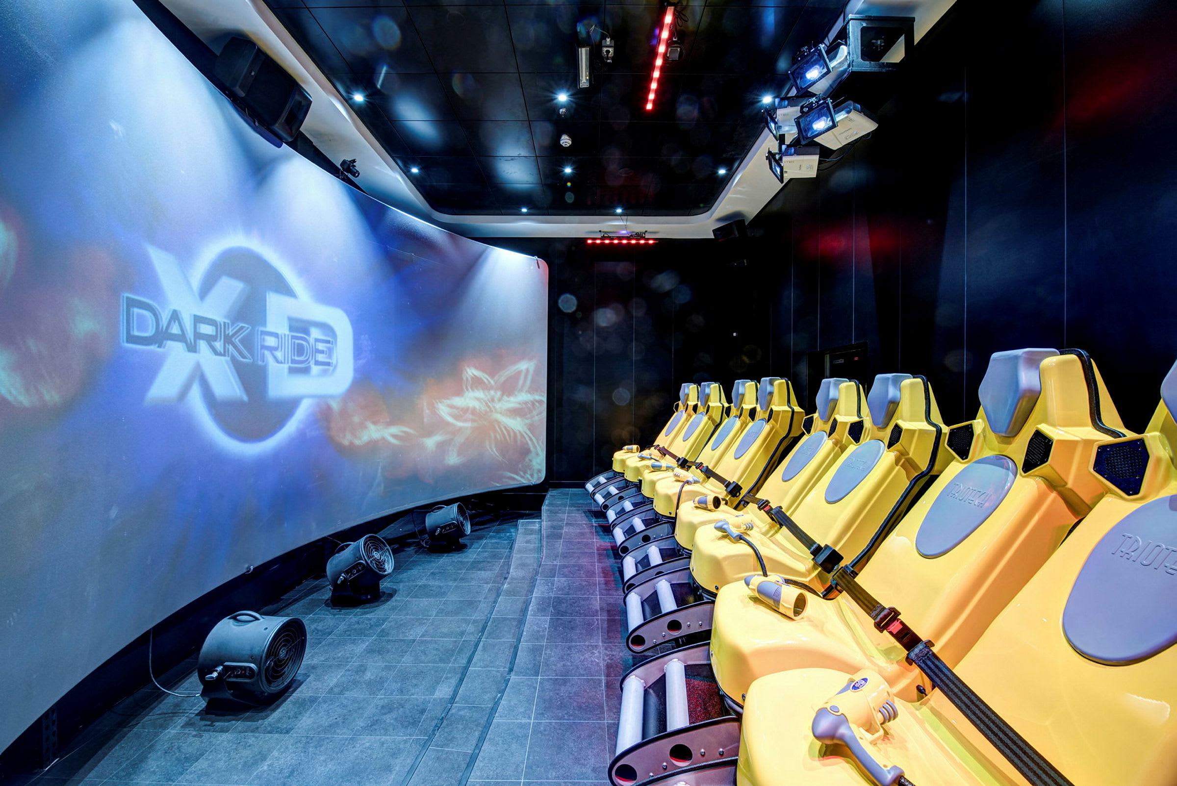 Rad av gula säten framför en stor välvd skärm med texten "XD Dark Ride". (AI-genererad text)