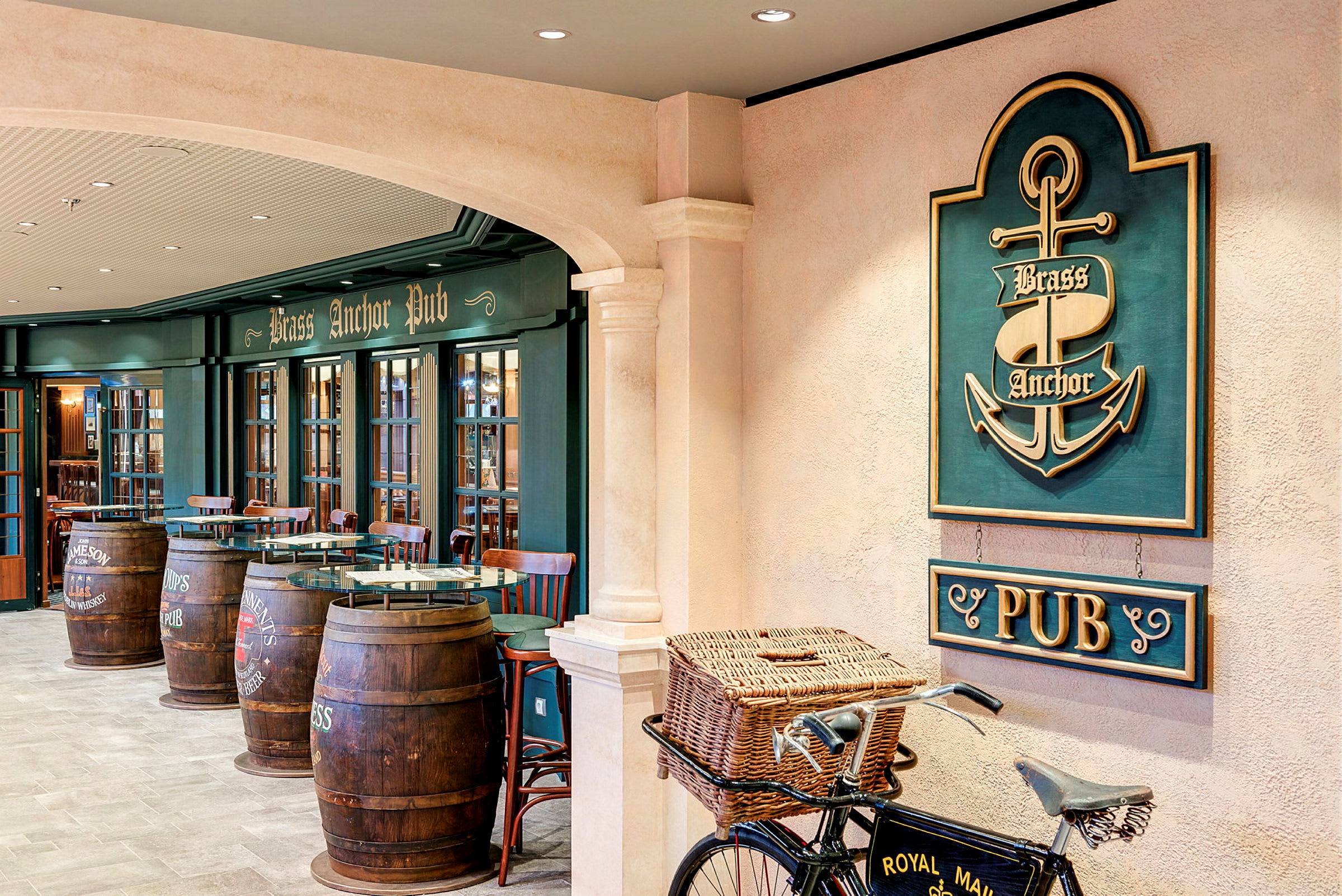 Interiör av en pub med en skylt som säger 'Brass Anchor Pub', trämöbler och fat som används som bord, samt en cykel med en korg framtill. (AI-genererad text)