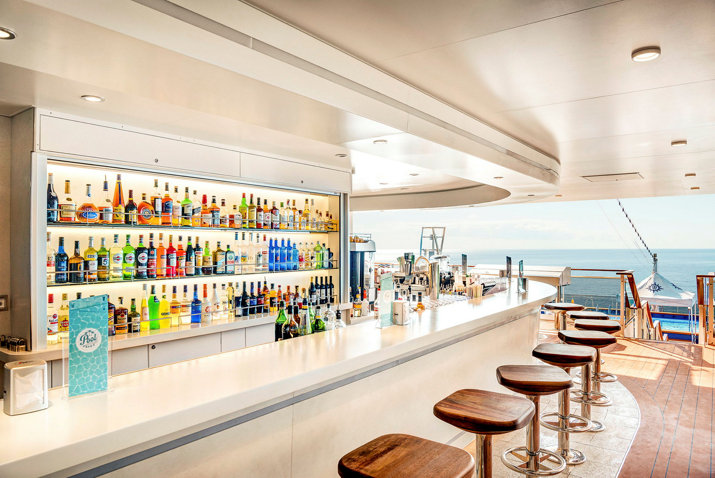 En bar med alkoholflaskor och stolar vid en havsutsikt. (AI-genererad text)