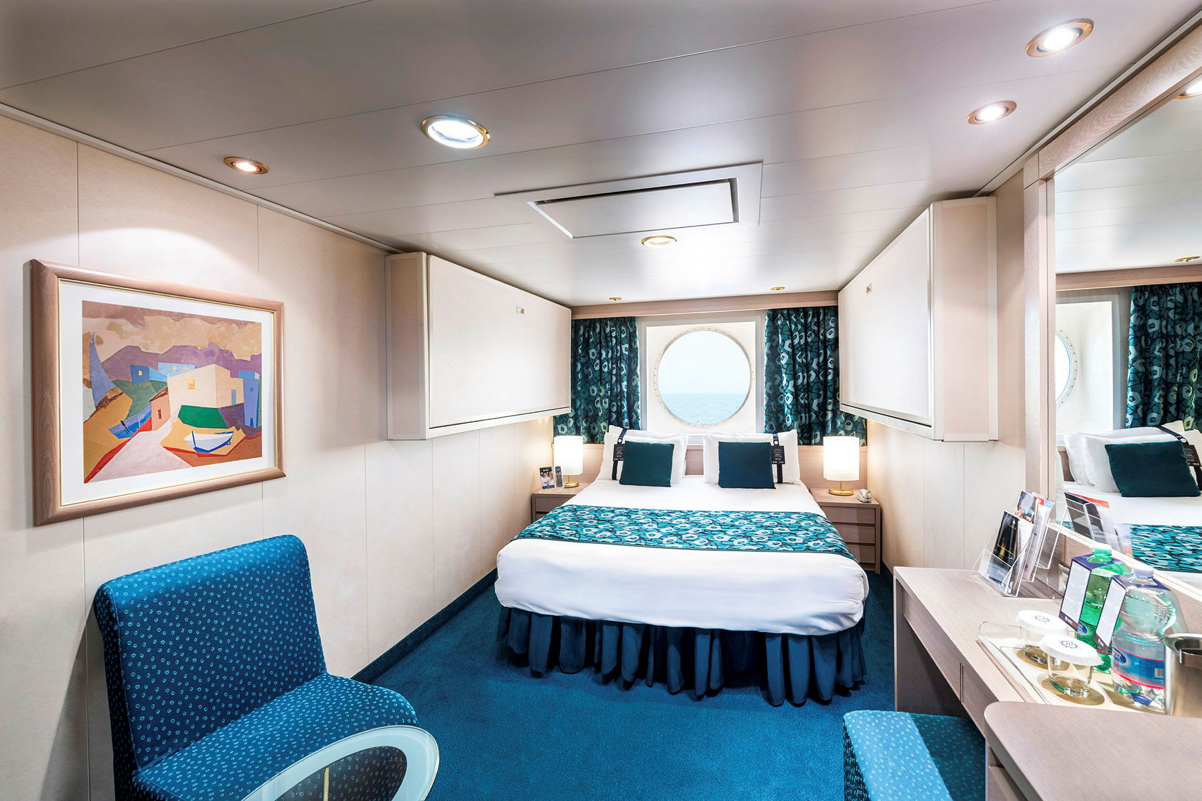 Ett välmöblerat hotellrum med en dubbelsäng, en stol och en rund fönstervy mot havet. (AI-genererad text)