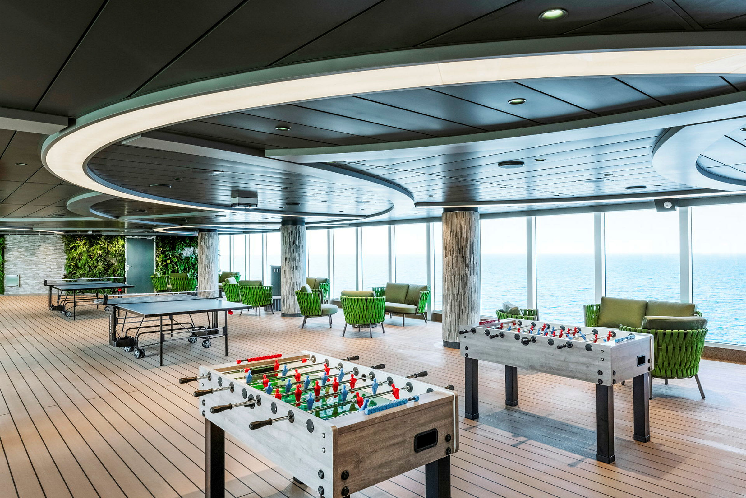 Ett rymligt rum med bordtennisbord och foosballbord, omgiven av stora fönster med utsikt över havet. (AI-genererad text)
