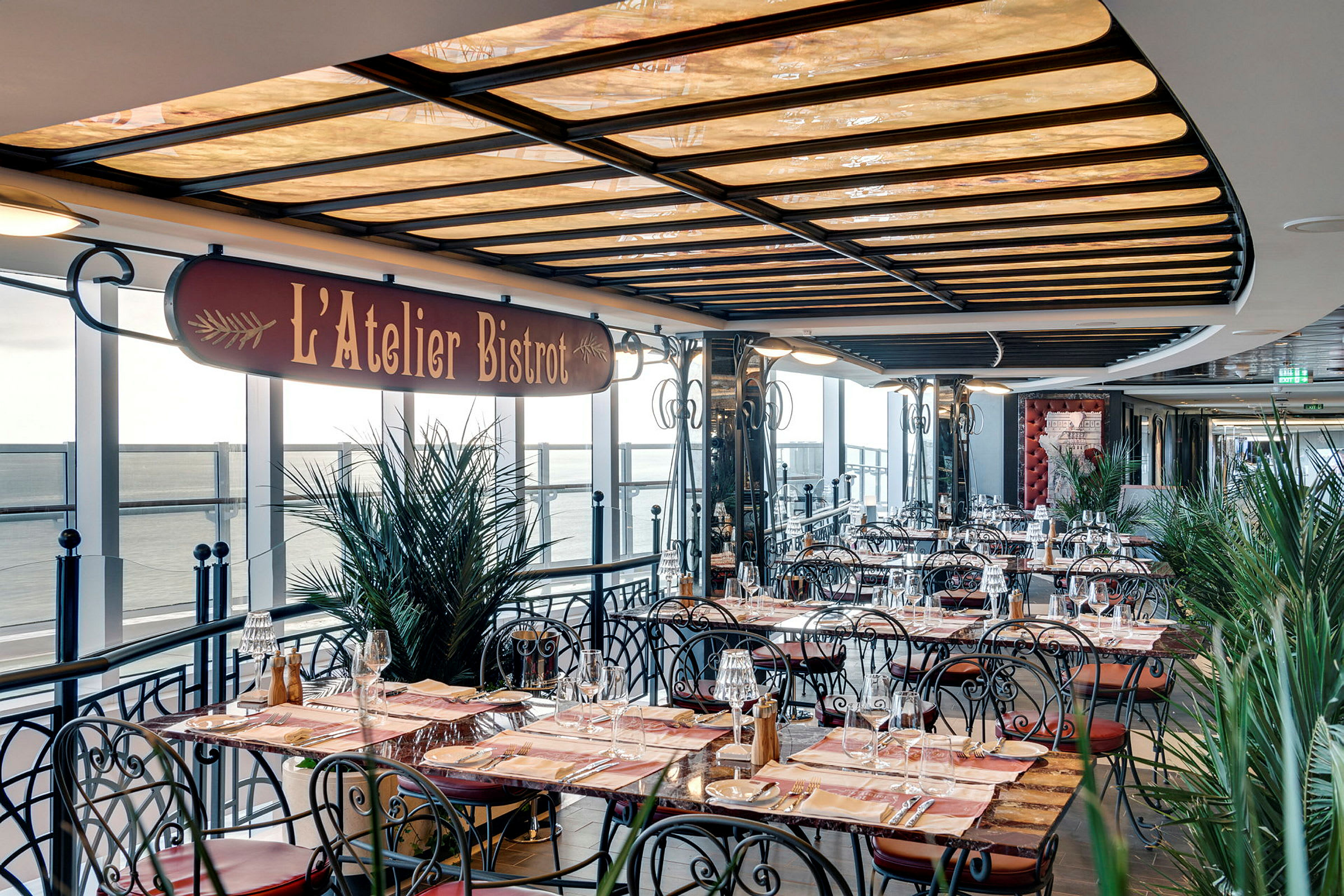 Uteserveringen av restaurangen L'Atelier Bistro med bord och stolar med havsutsikt. (AI-genererad text)