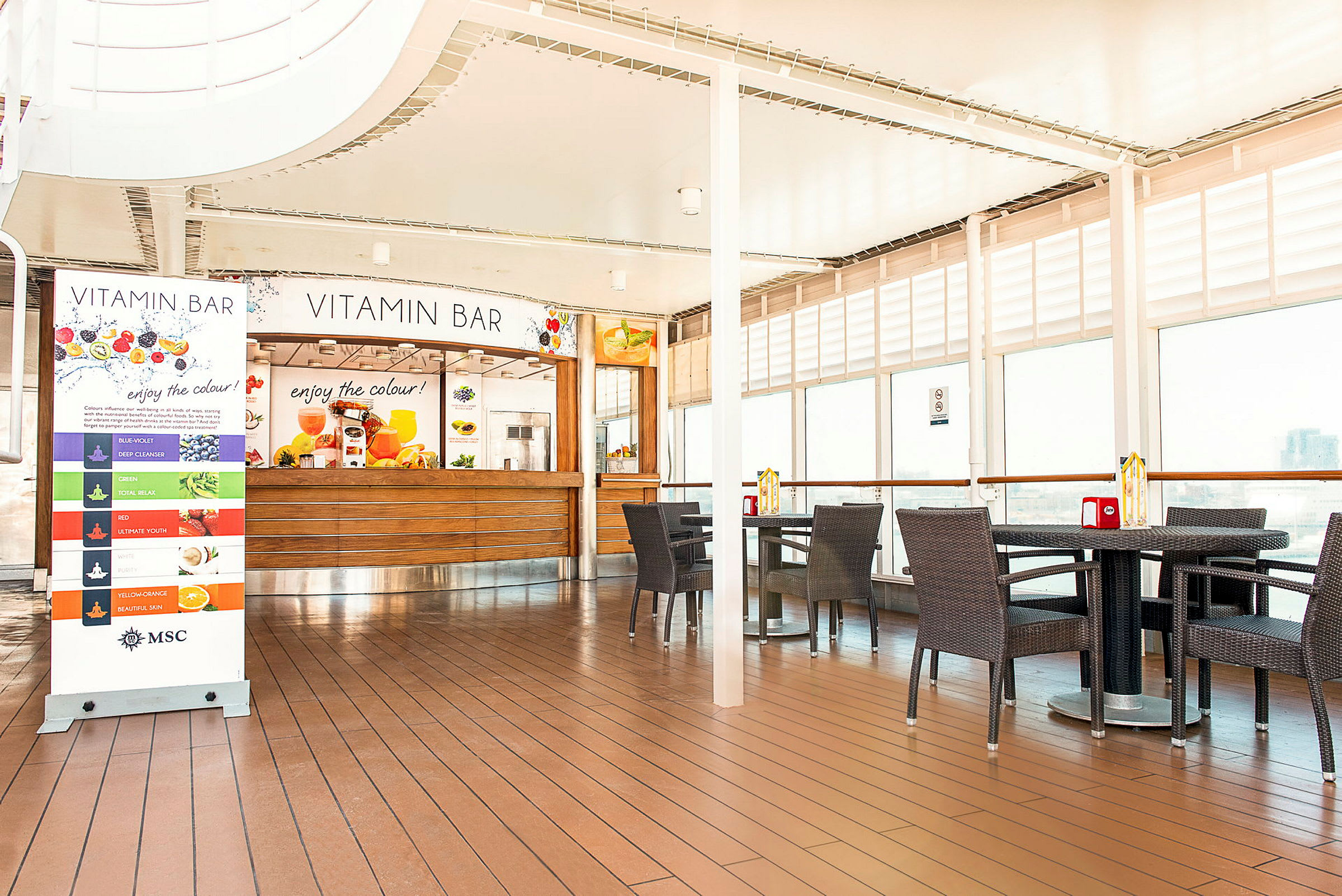 Inomhusmiljö med en juicebar med namnet Vitamin Bar, omgiven av bord och stolar. (AI-genererad text)