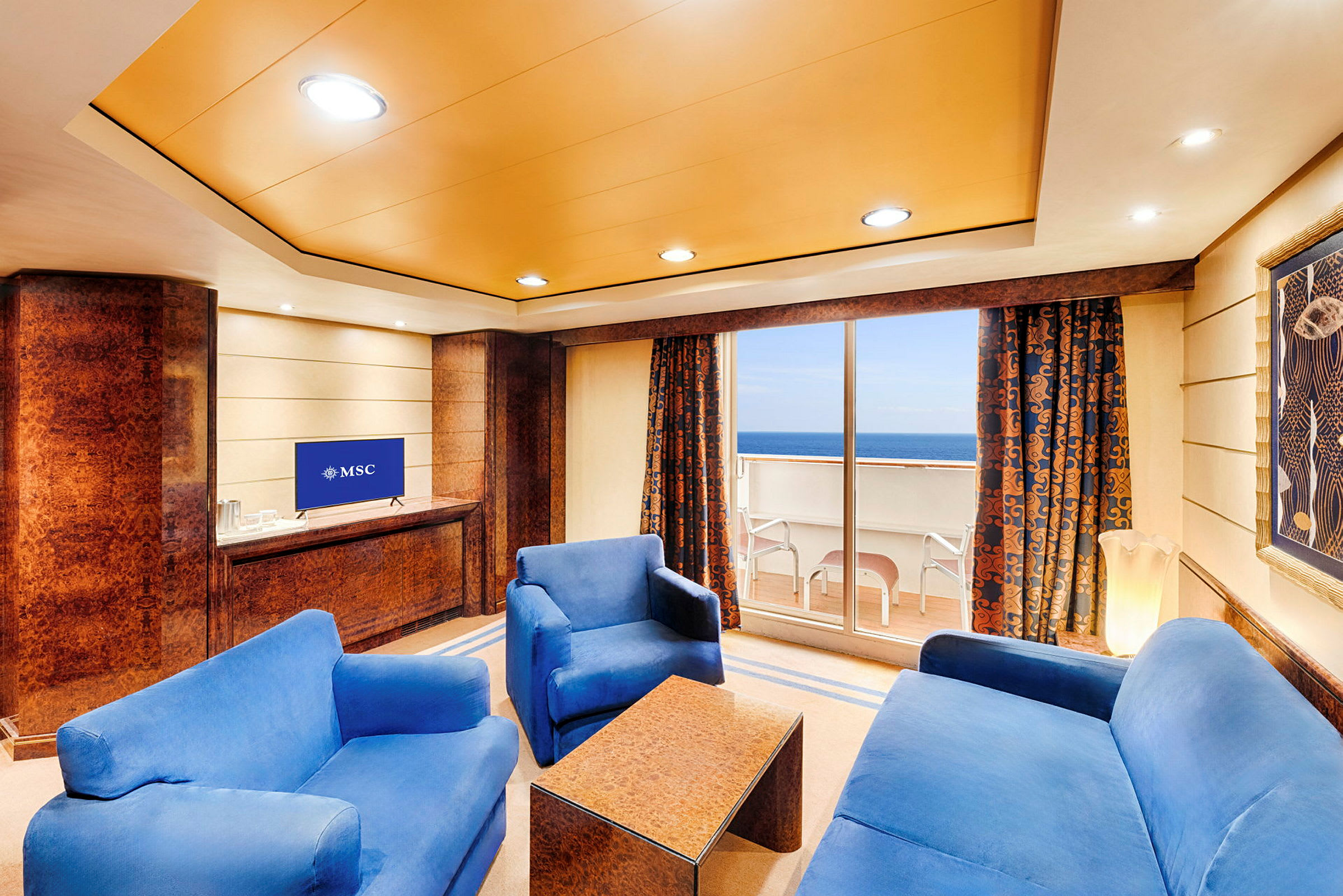 Ett vardagsrum med blå soffor, ett soffbord, en TV och en balkong med utsikt över havet. (AI-genererad text)