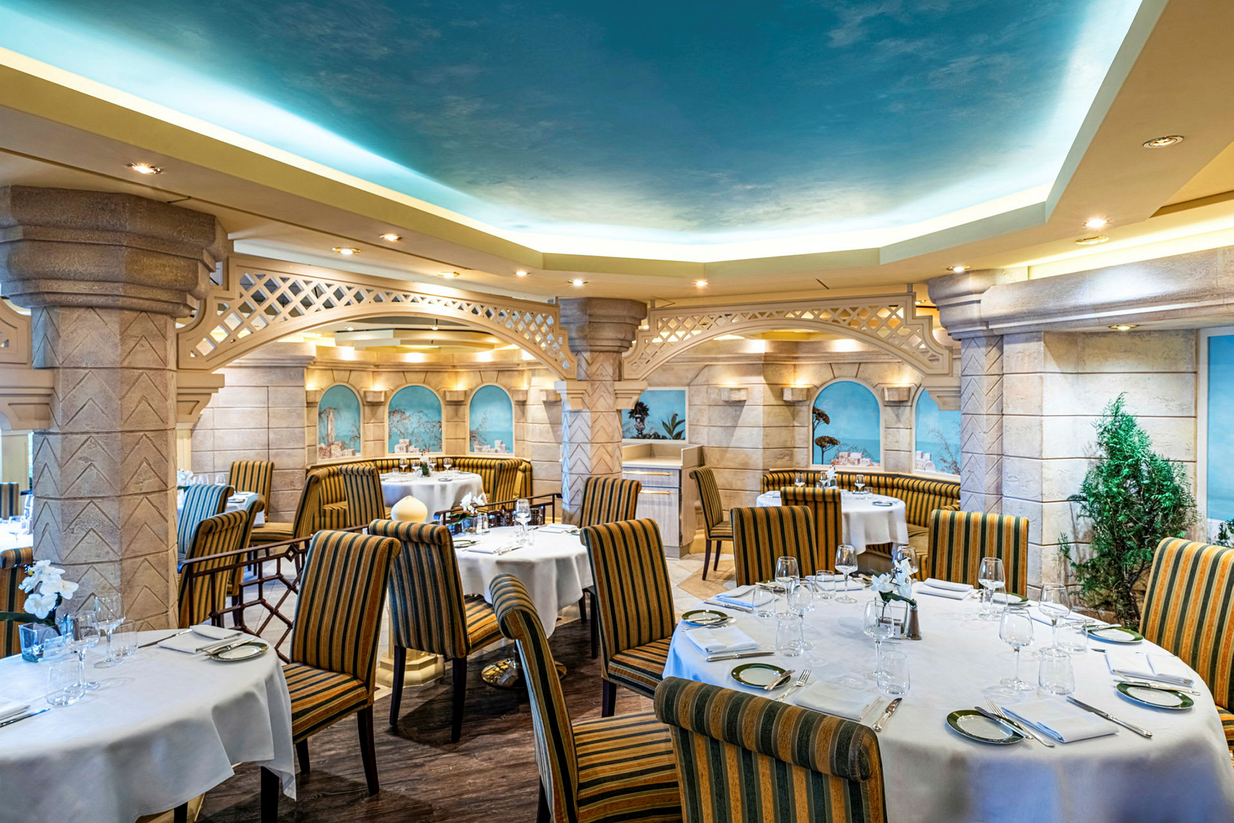 Interiör av en restaurang med rundade tak, dekorerade väggar, dukade bord och randiga stolar. (AI-genererad text)