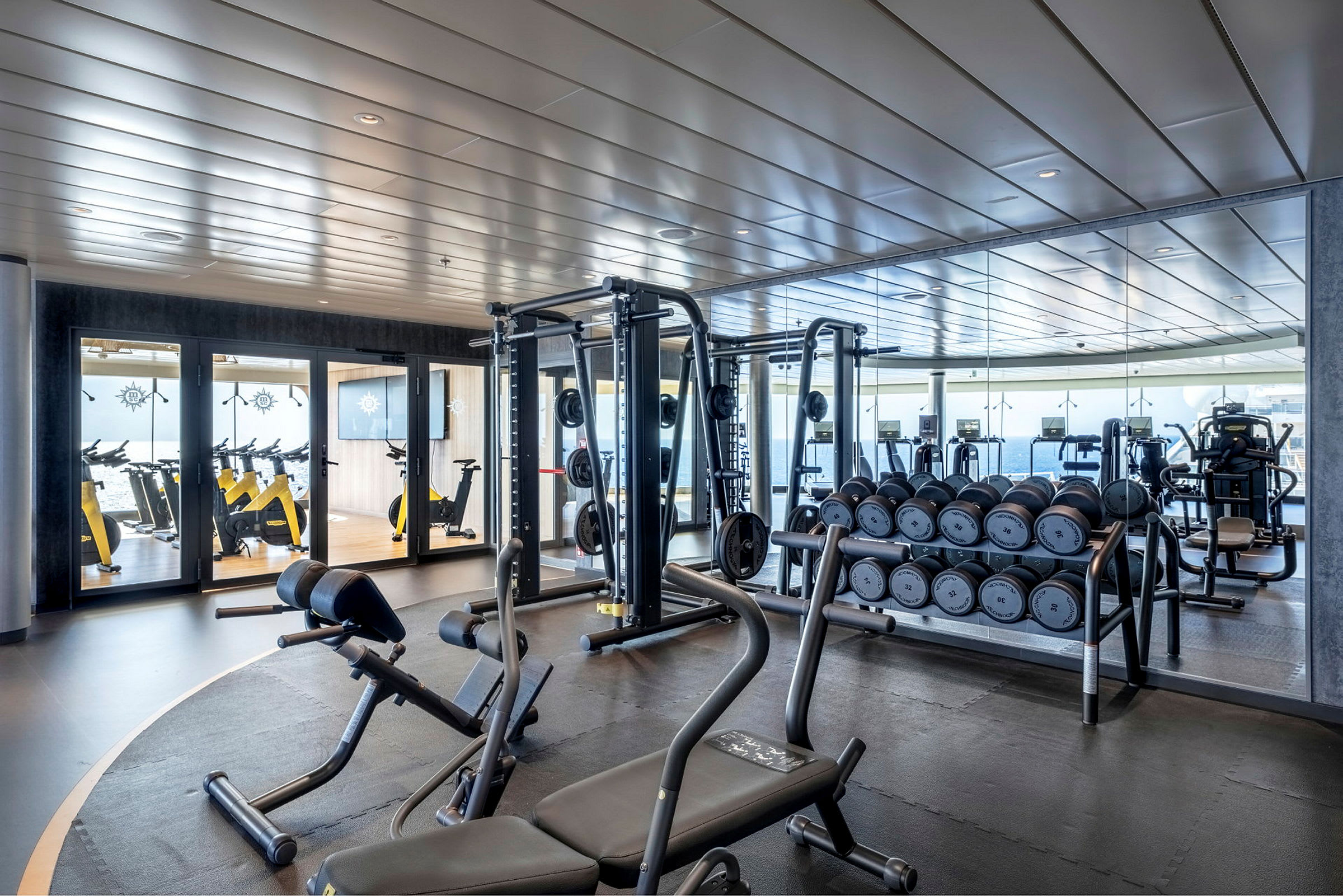 Bild på ett gym med träningsutrustning, hantlar och speglar. (AI-genererad text)